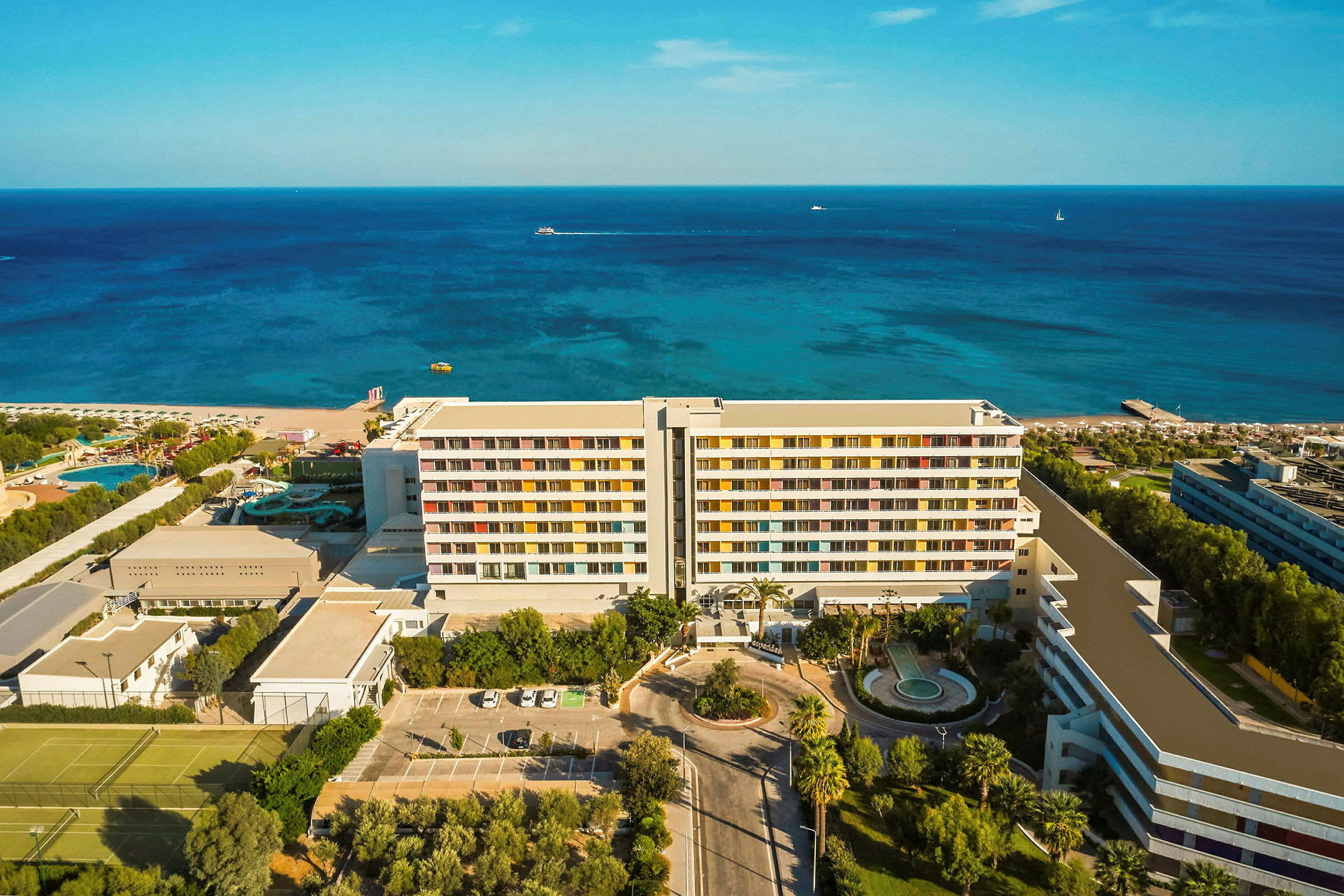 Lentokuva hotellista rannalla, taustalla meri ja hiekkaranta. (Tekoälyn luoma teksti)