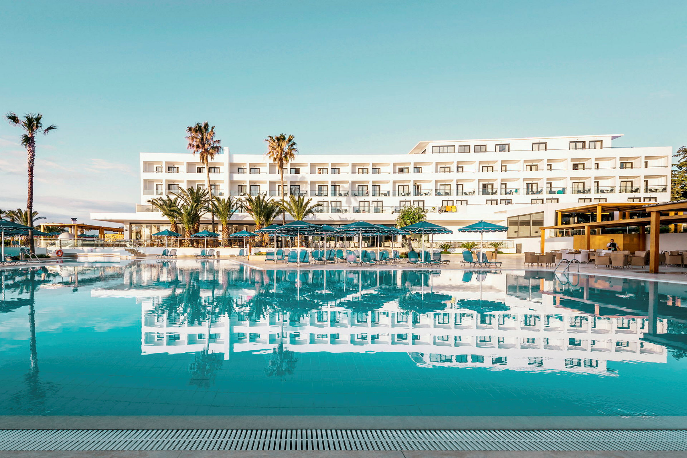 Hotellirakennus, jossa uima-allas ja aurinkotuoleja etualalla. (Tekoälyn luoma teksti)