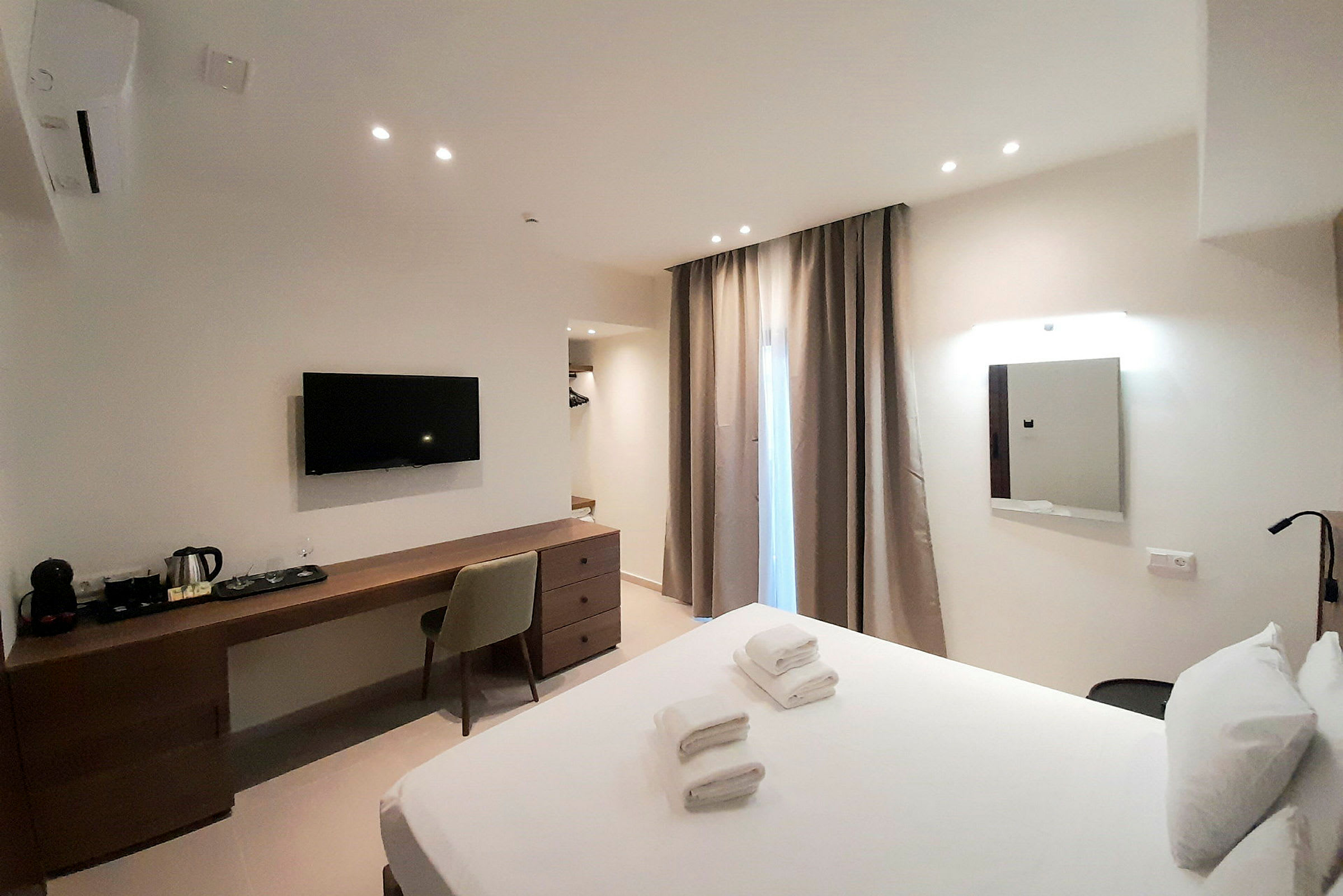 Hotellihuone, jossa on pedattu sänky, kirjoituspöytä tuolilla, seinään kiinnitetty TV ja verhot ikkunan edessä. (Tekoälyn luoma teksti)
