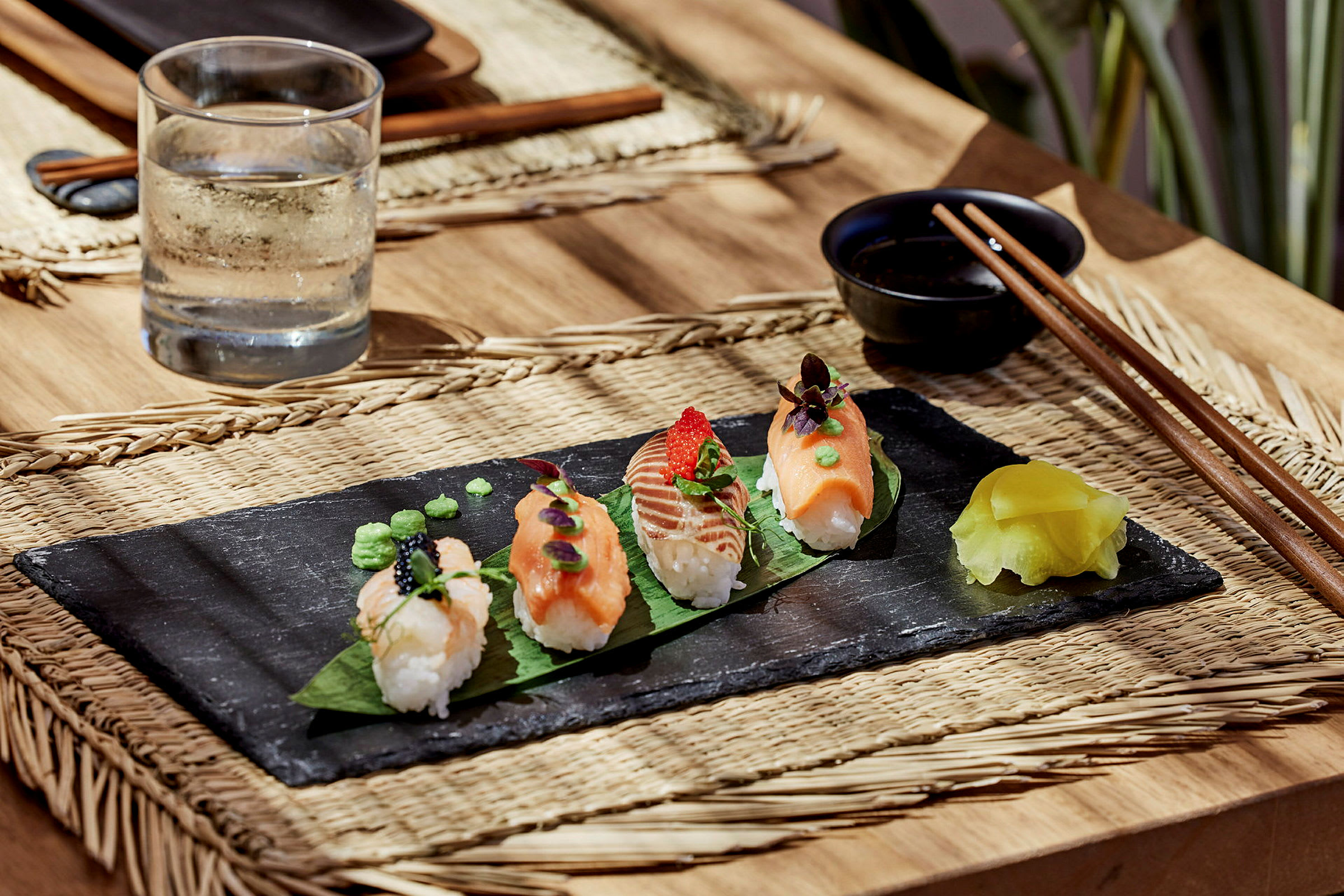 Sushipaloja mustalla lautasella kannun vettä ja syömäpuikkojen vieressä. (Tekoälyn luoma teksti)