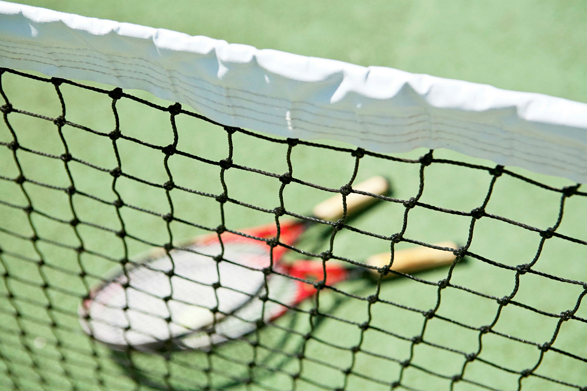 Lähikuva tenniskentän verkosta, jonka takana kaksi tennismailaa kentällä. (Tekoälyn luoma teksti)