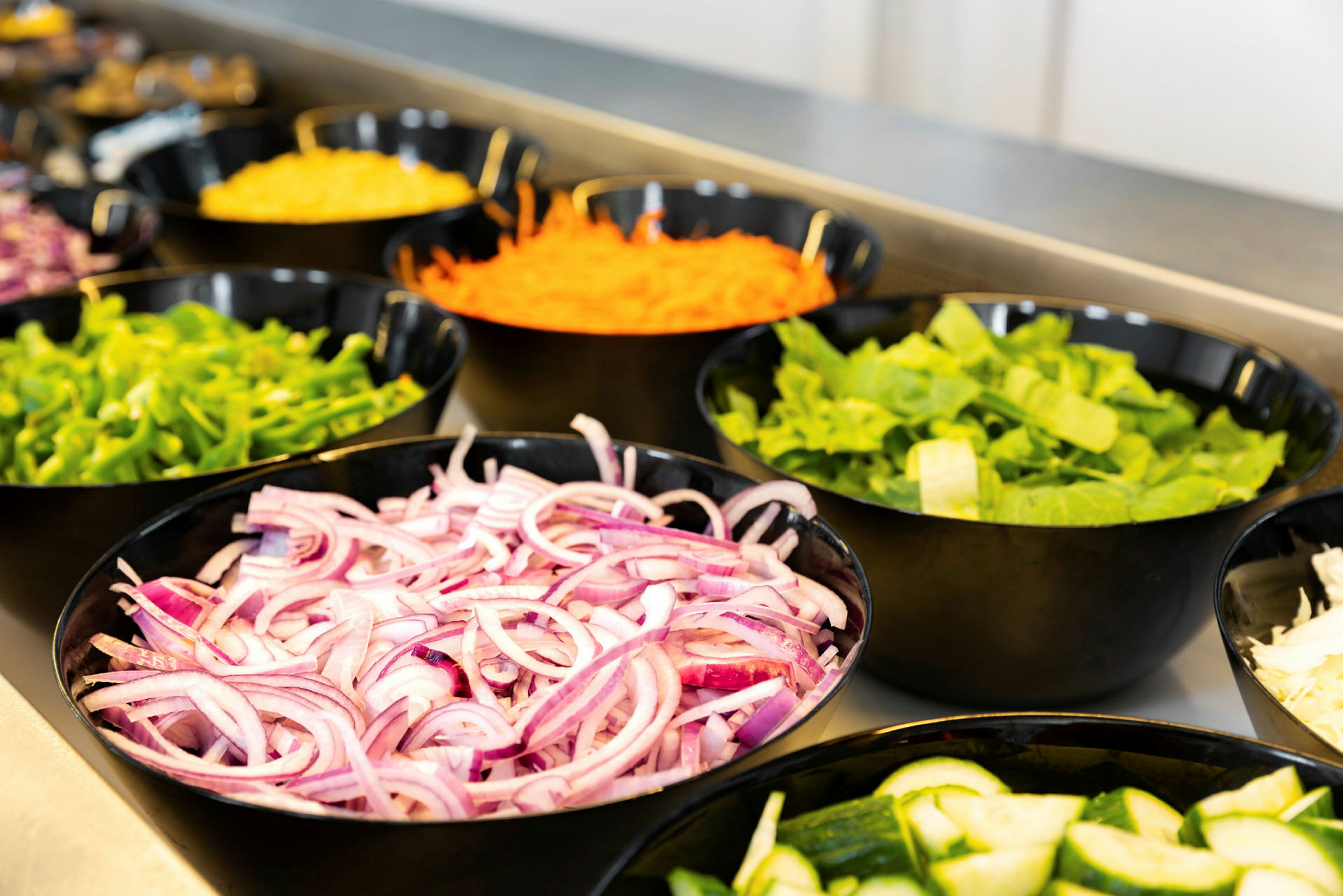Kulhot, joissa on erilaisia vihanneksia, kuten punasipulia, kurkkua, salaattia, paprikaa ja porkkanaraastetta. (Tekoälyn luoma teksti)