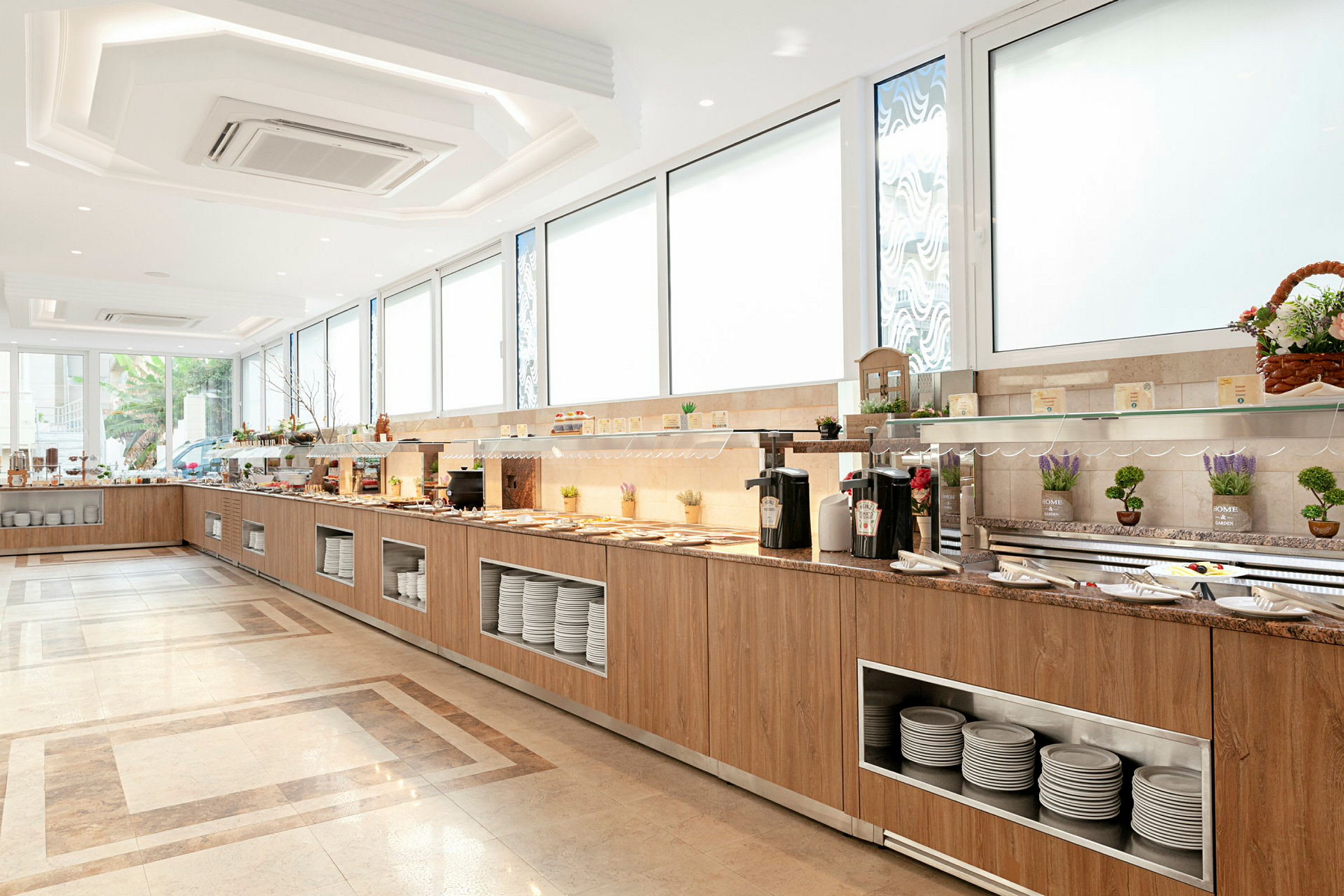 Buffet-alue, jossa tarjoilutiskit ja lautashyllyt valoisassa ja modernissa ympäristössä. (Tekoälyn luoma teksti)