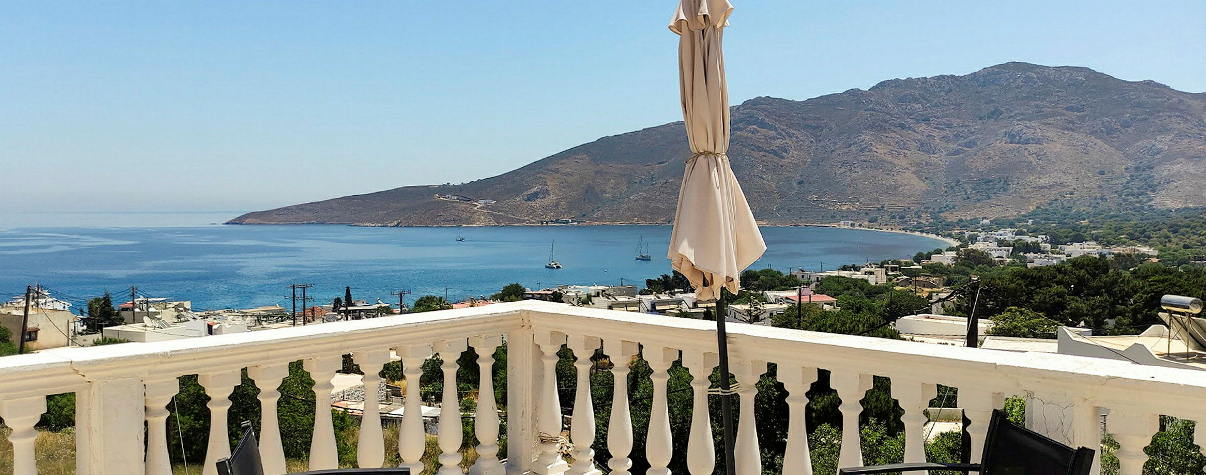 Näkymä terassilta, jossa kaiteet, aurinkovarjo sekä meri ja vuoret taustalla. (Tekoälyn luoma teksti)