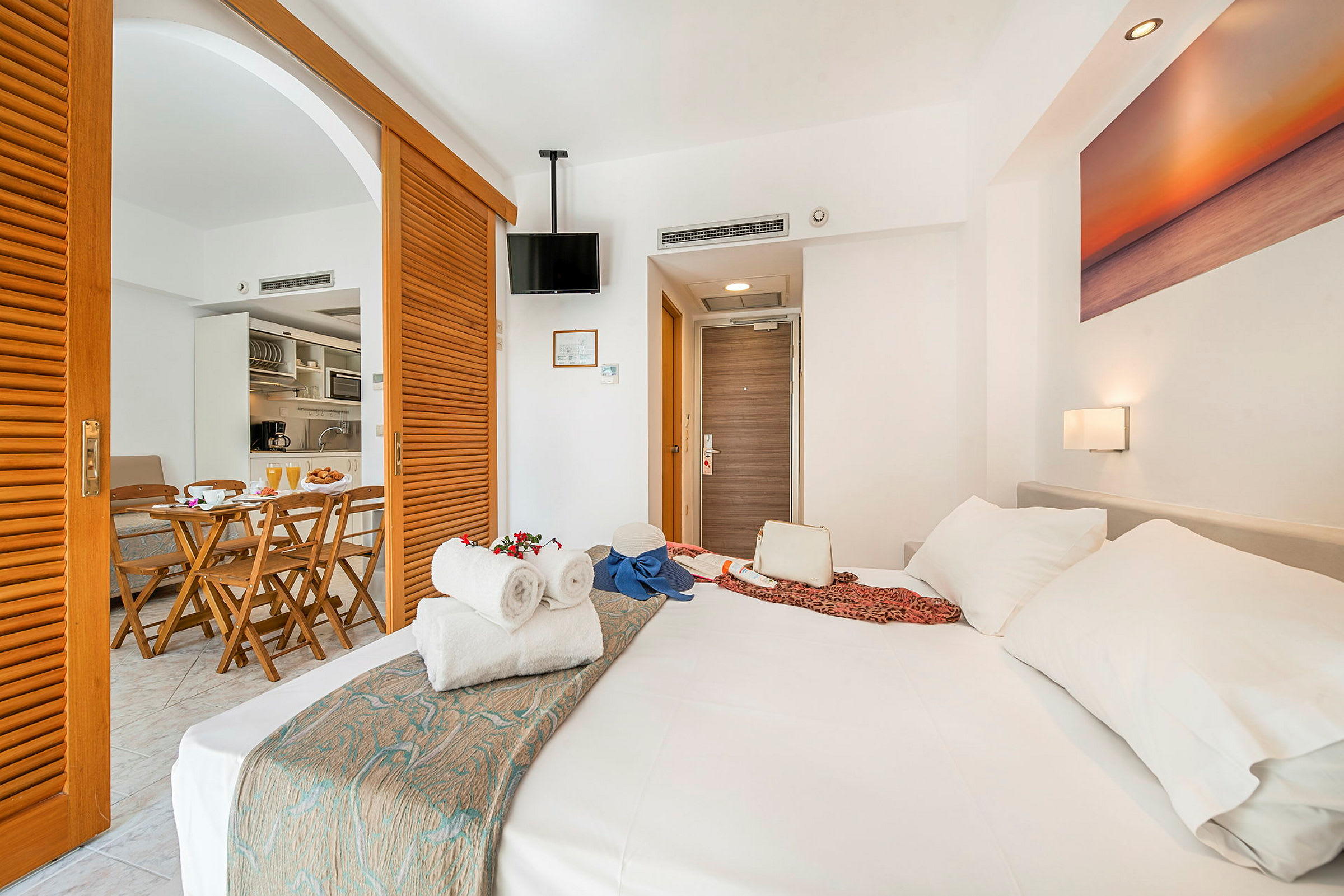 Hotellihuone, jossa on pedattu sänky ja ruokailutila keittiöllä taustalla. (Tekoälyn luoma teksti)
