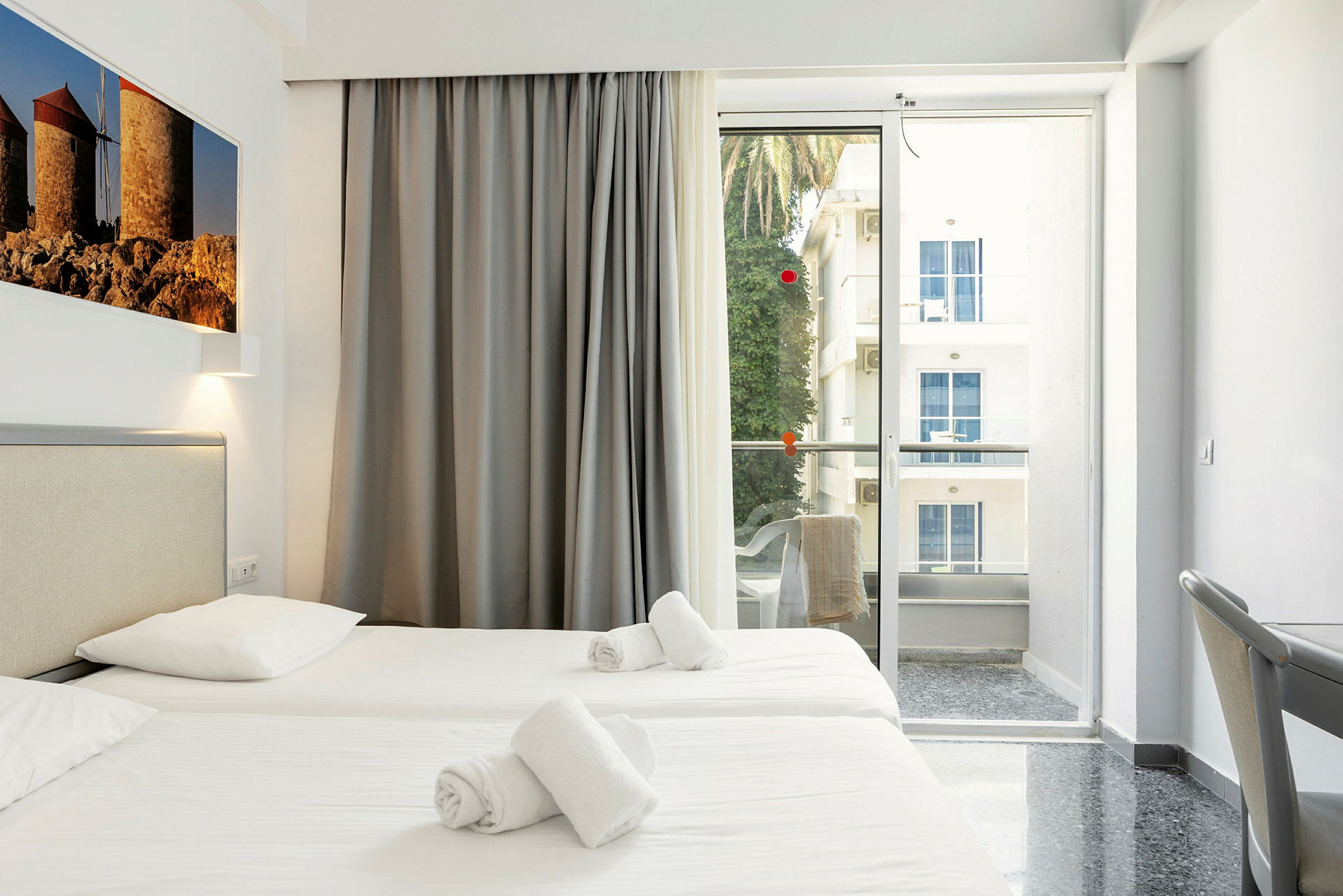 Hotellihuone, jossa on kaksi yhden hengen vuodetta, parveke näkymällä. (Tekoälyn luoma teksti)
