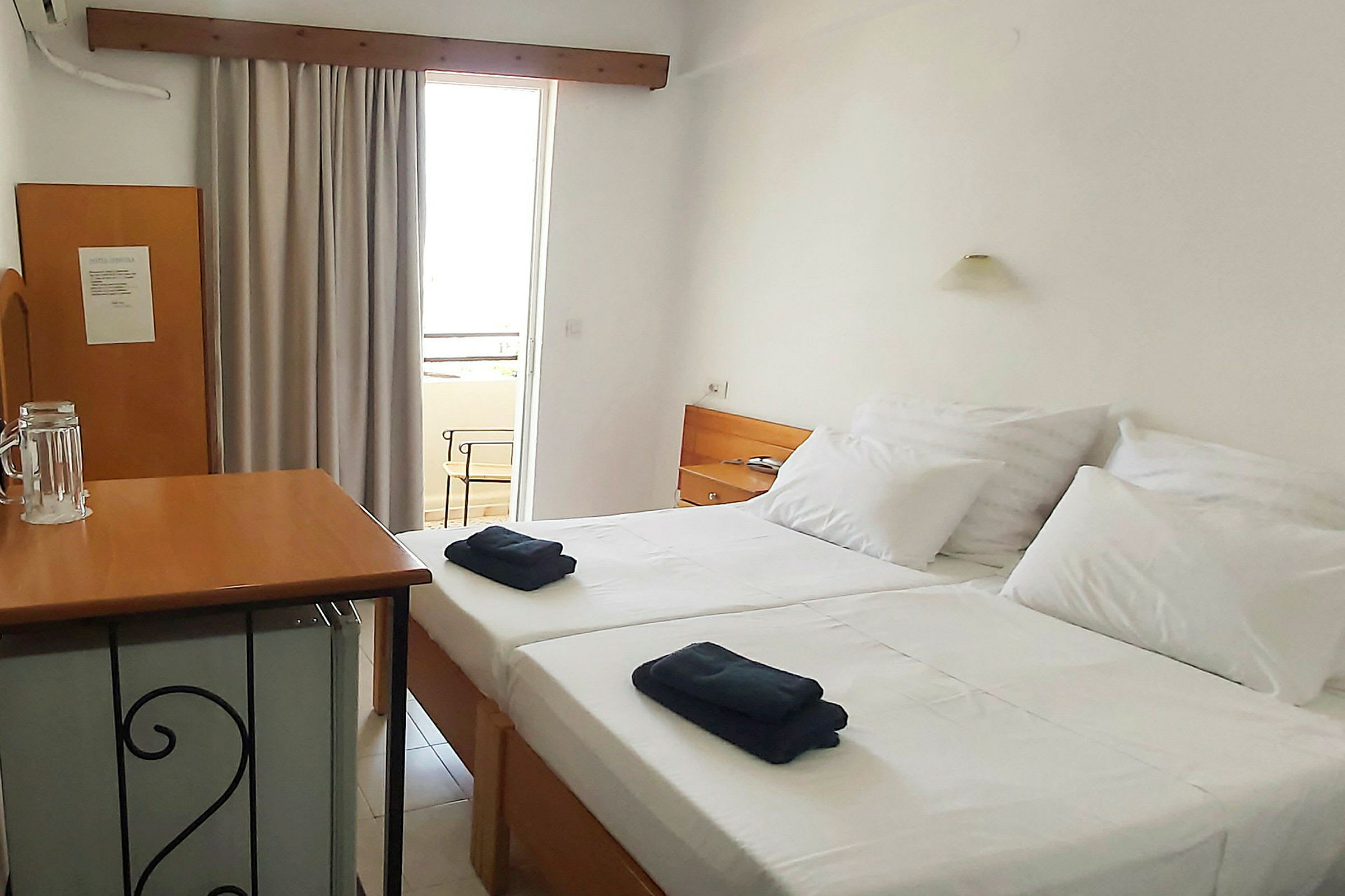 Hotellihuone, jossa on kaksi erillistä vuodetta, pieni pöytälevy ja ovi, joka johtaa parvekkeelle. (Tekoälyn luoma teksti)