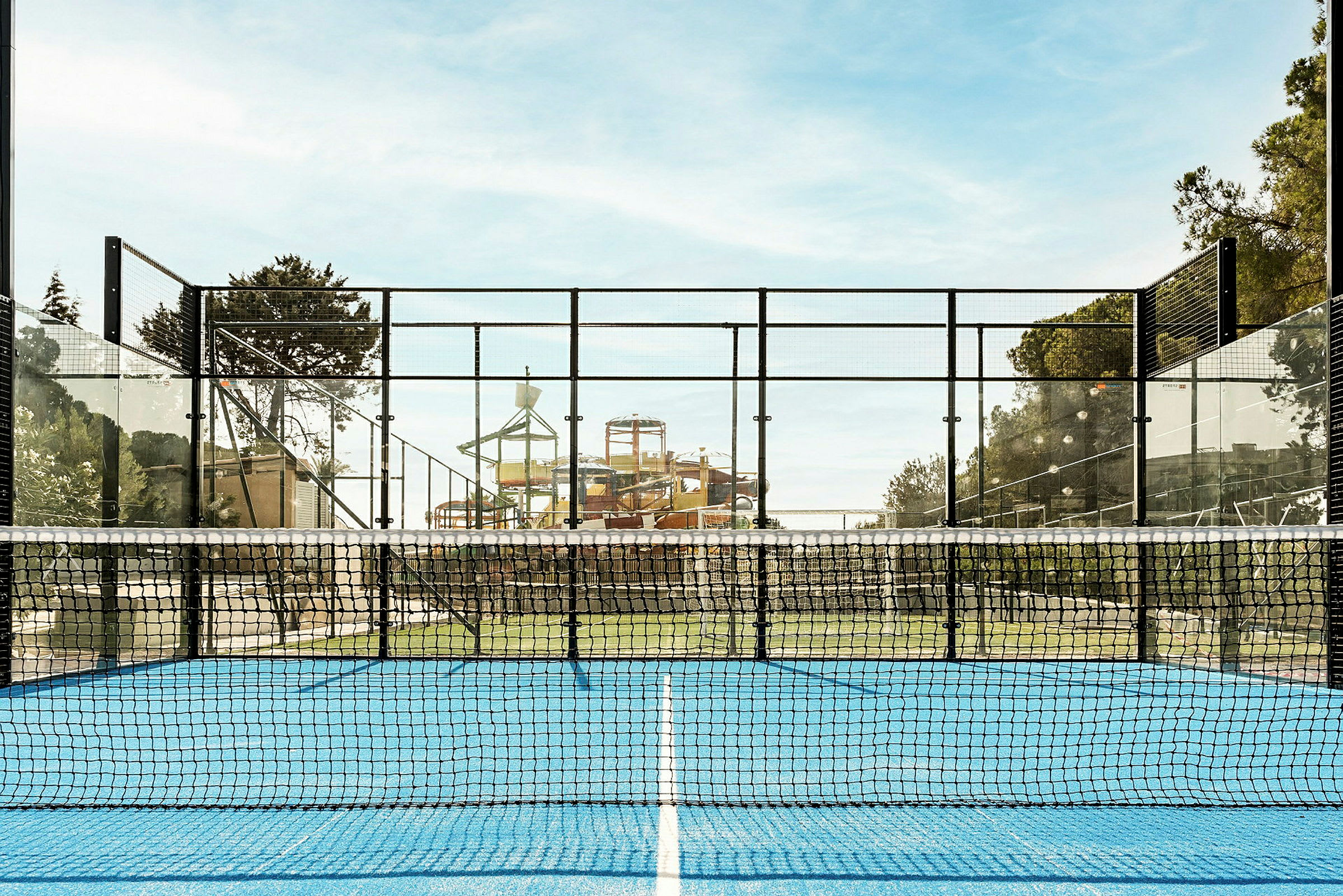 Sininen alusta ja verkko etualalla oleva padelhalli, taustalla vesipuisto. (Tekoälyn luoma teksti)