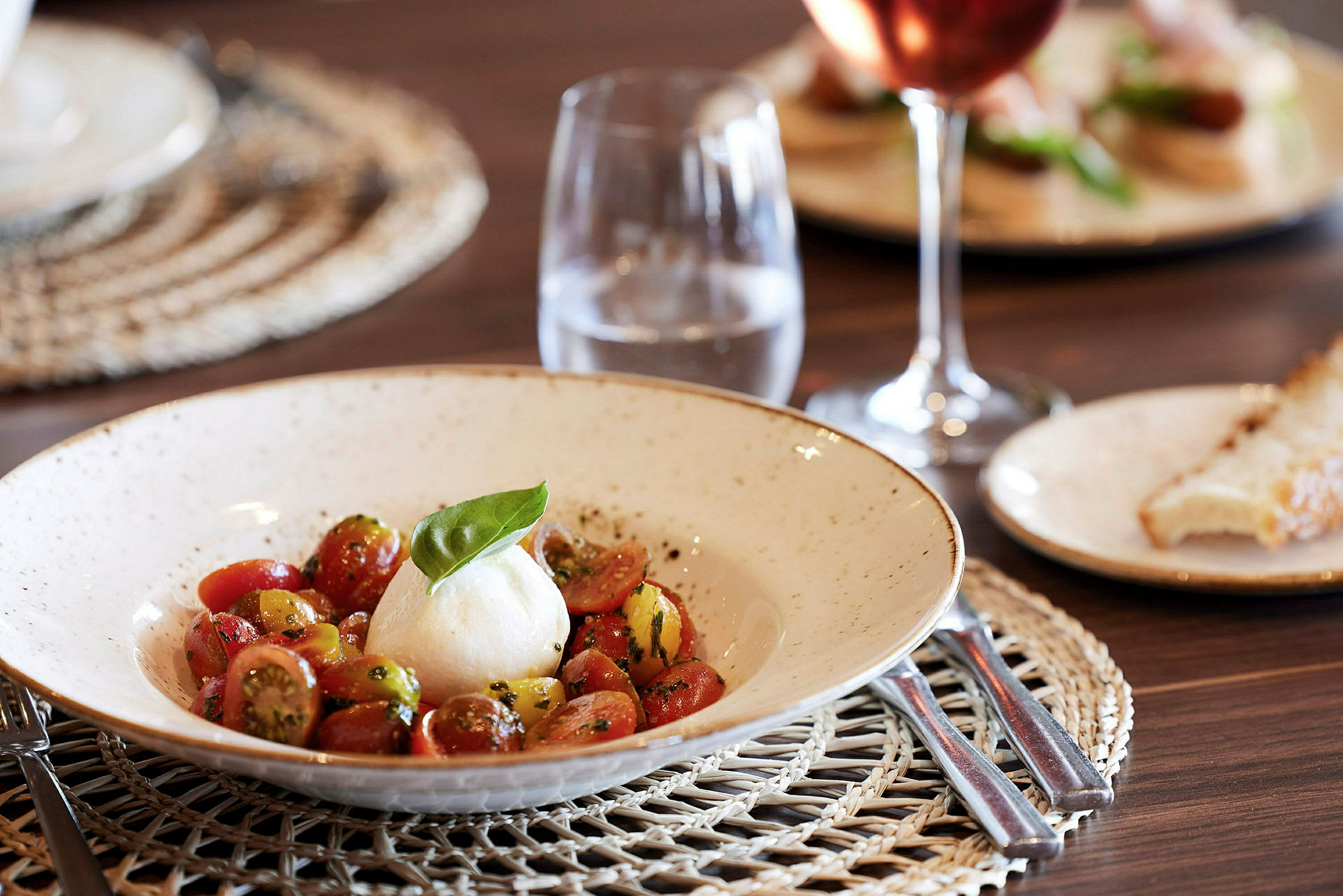 Lautanen mozzarella- ja tomaattisalaattia sekä vesilasi pöydällä. (Tekoälyn luoma teksti)