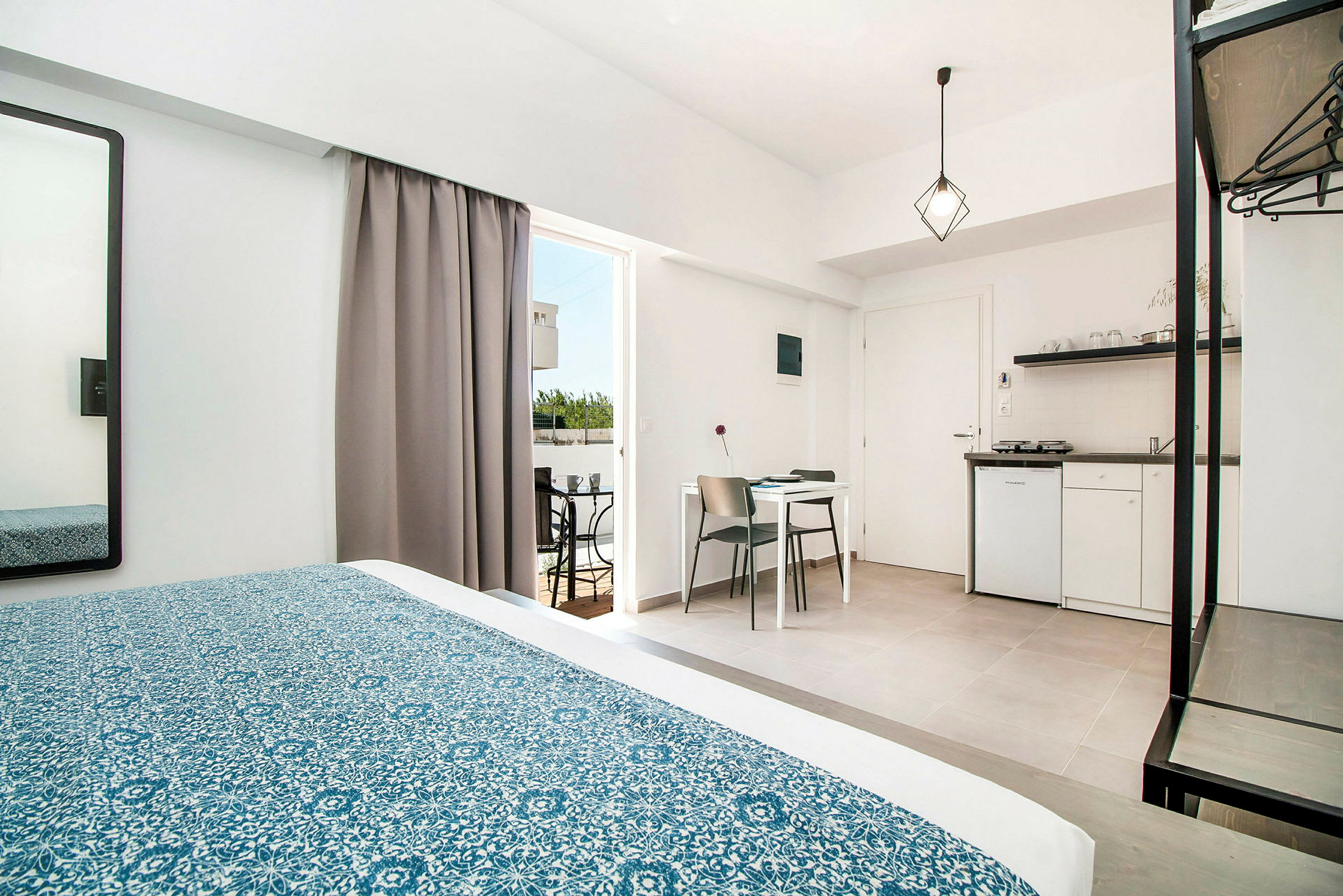Hotellihuone, jossa on sänky, pöytä, tuolit ja pieni keittiö. (Tekoälyn luoma teksti)