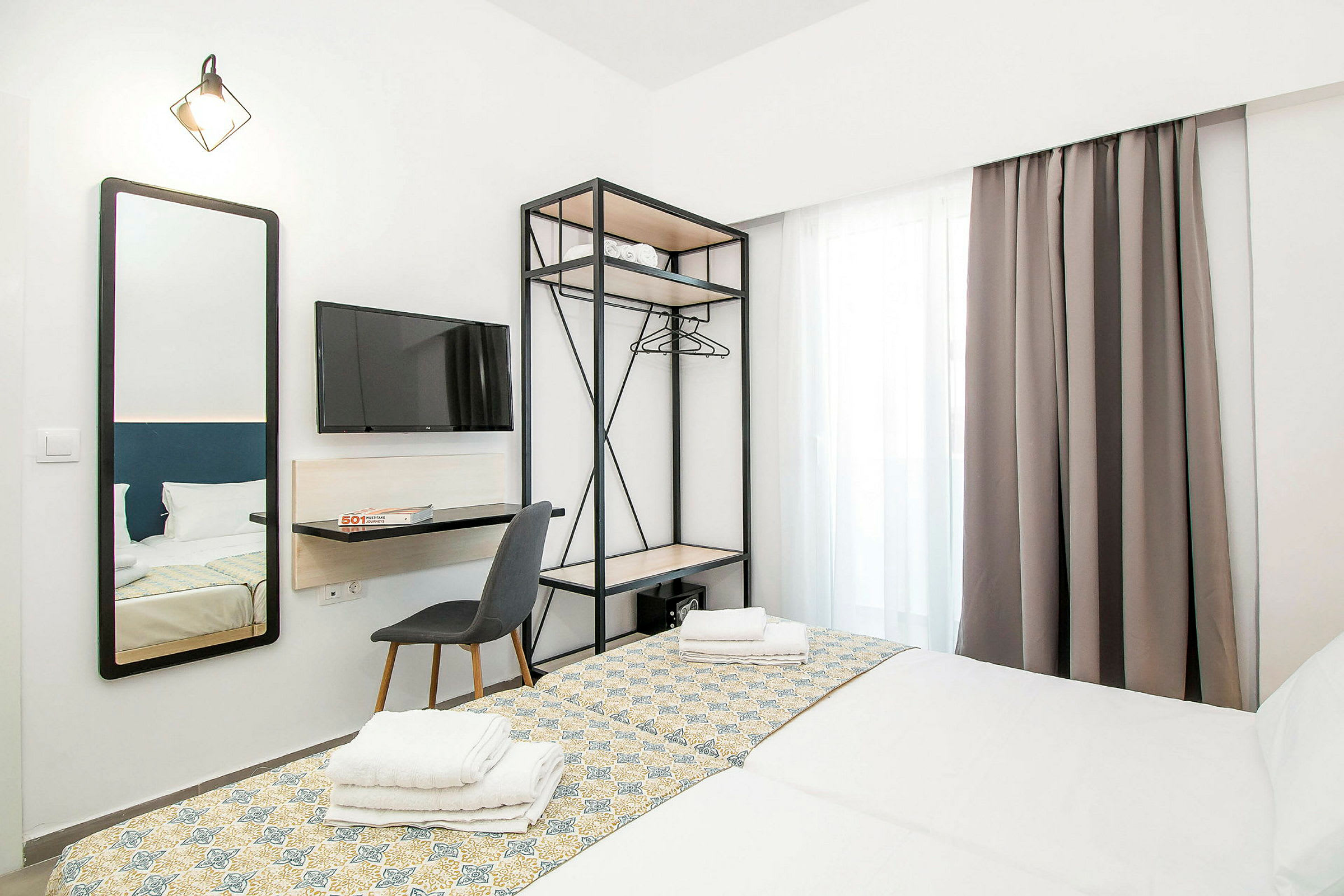 Hotellihuone, jossa on kaksi pedattua sänkyä, seinään kiinnitetty televisio, peili ja avoin vaatekaappi. (Tekoälyn luoma teksti)
