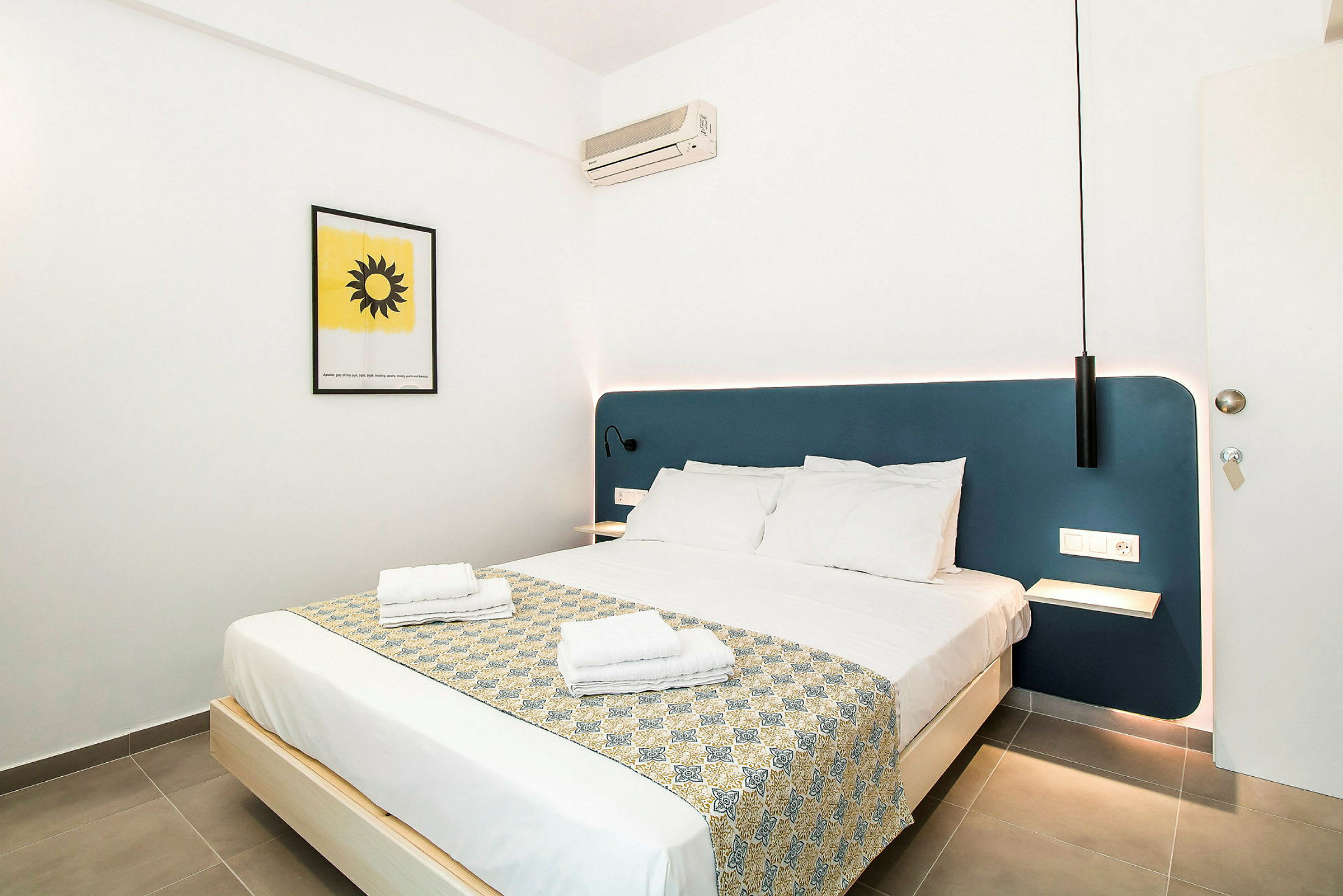 Hotellihuone, jossa parivuode, sininen sängynpääty ja seinäkoriste. (Tekoälyn luoma teksti)