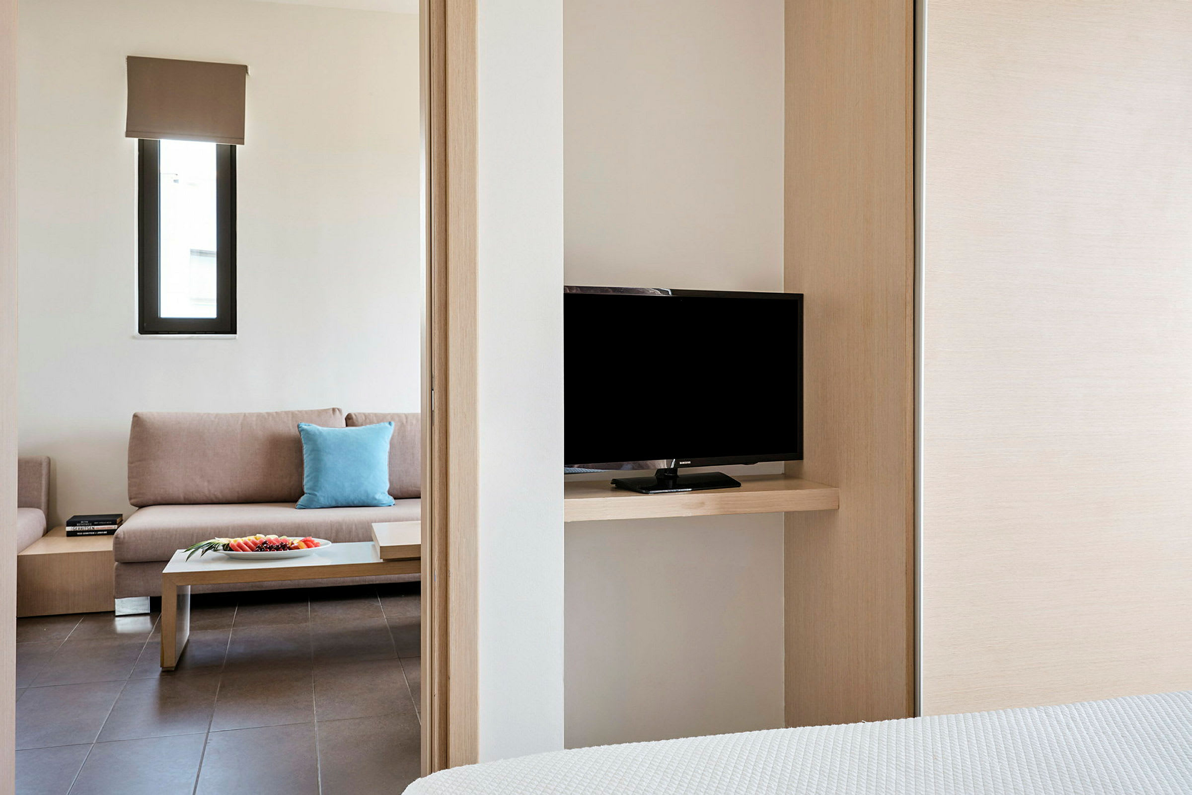 Hotellihuone, jossa on sohva, sivupöytä ja televisio näkyvissä makuuhuoneesta. (Tekoälyn luoma teksti)