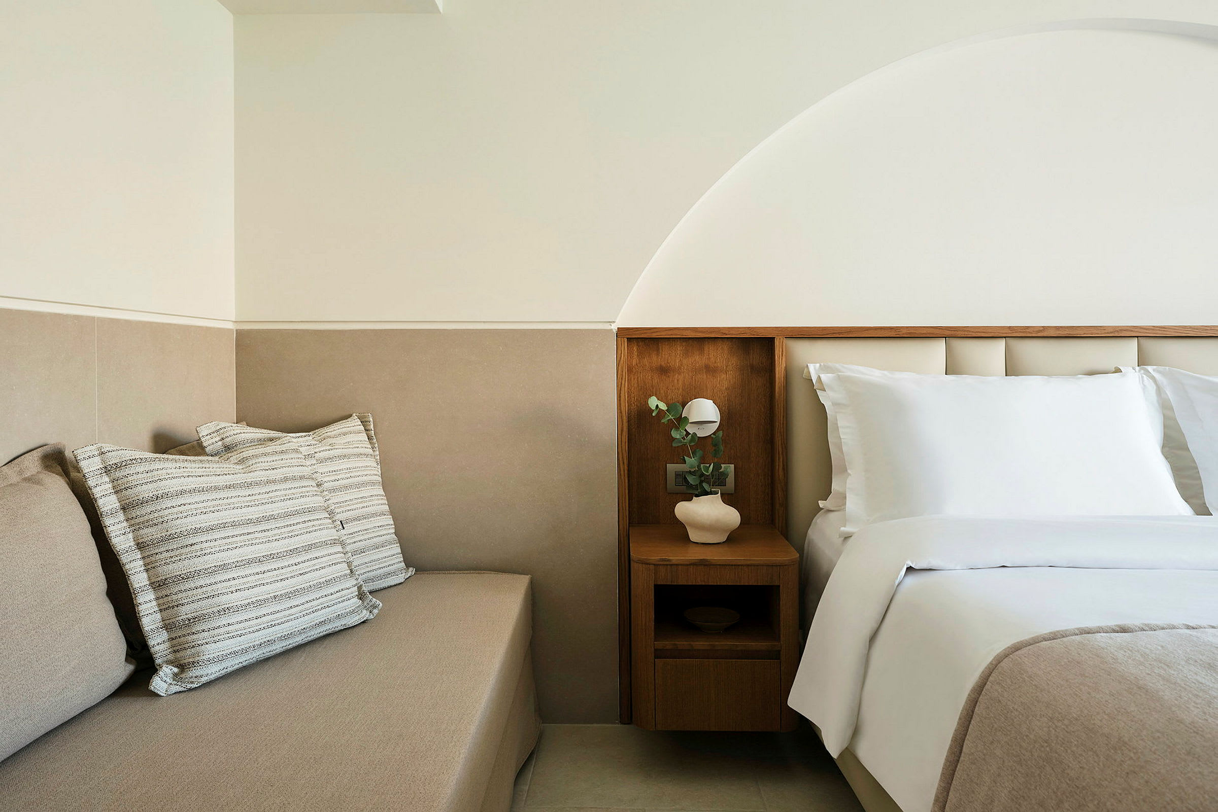 Vaalea ja moderni hotellihuone, jossa on pedattu sänky ja istumakaluste tyynyjen kera. (Tekoälyn luoma teksti)