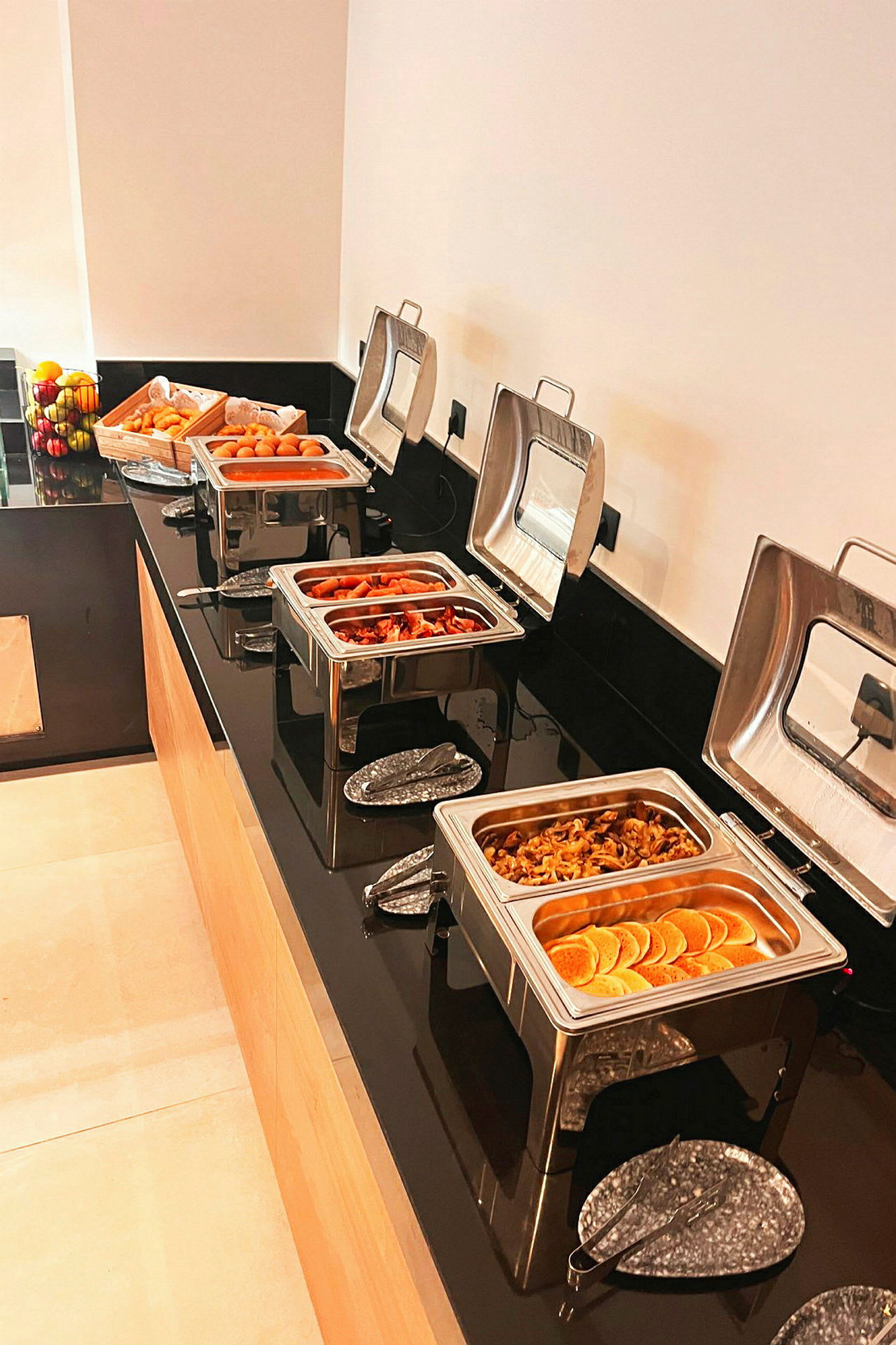 Buffet-pöytä lämpimällä ruoalla tarjoiluastioissa ja tuoreita hedelmiä vieressä. (Tekoälyn luoma teksti)