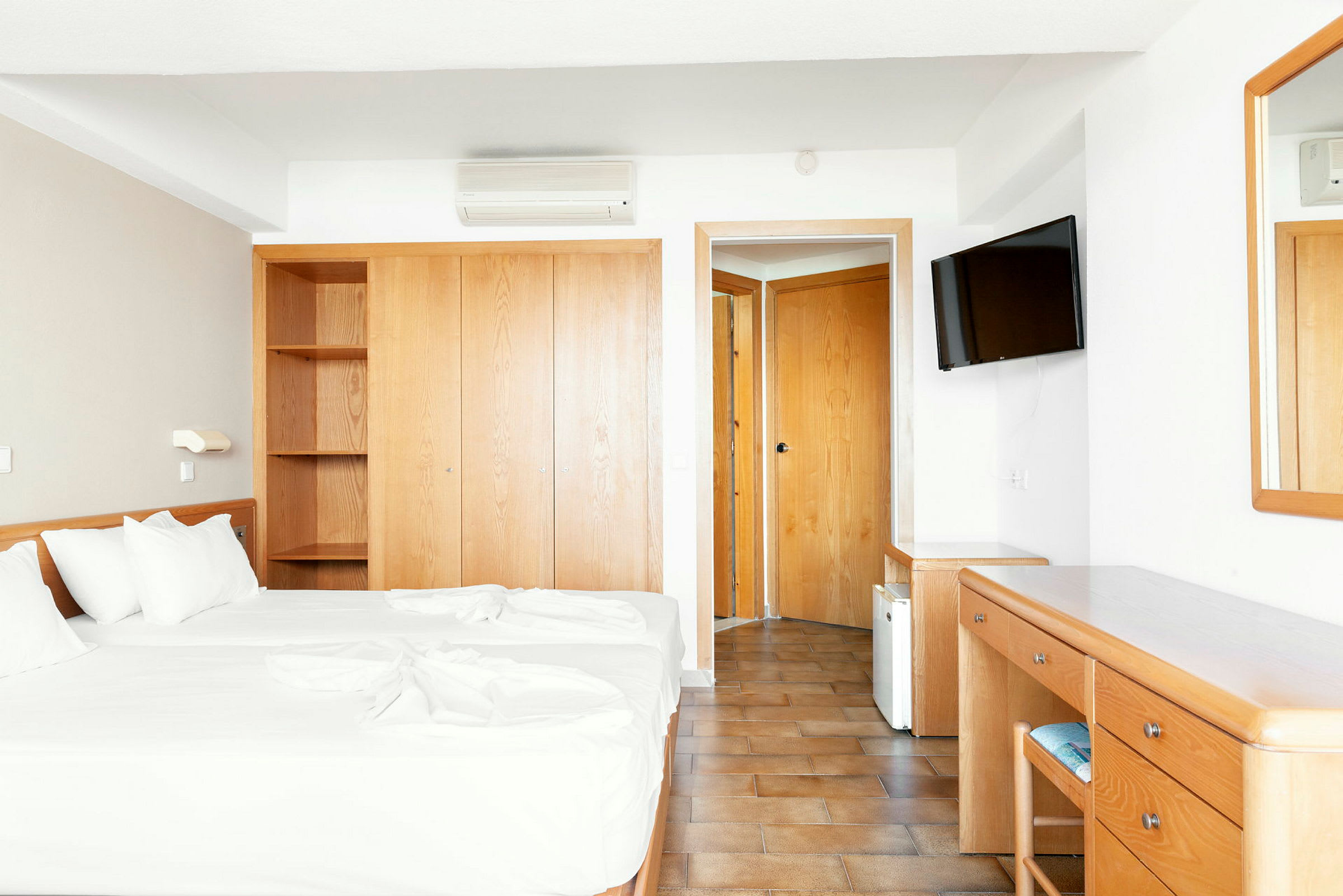 Hotellihuone, jossa on kaksi erillistä vuodetta, vaatekaappi, kirjoituspöytä ja peili. (Tekoälyn luoma teksti)