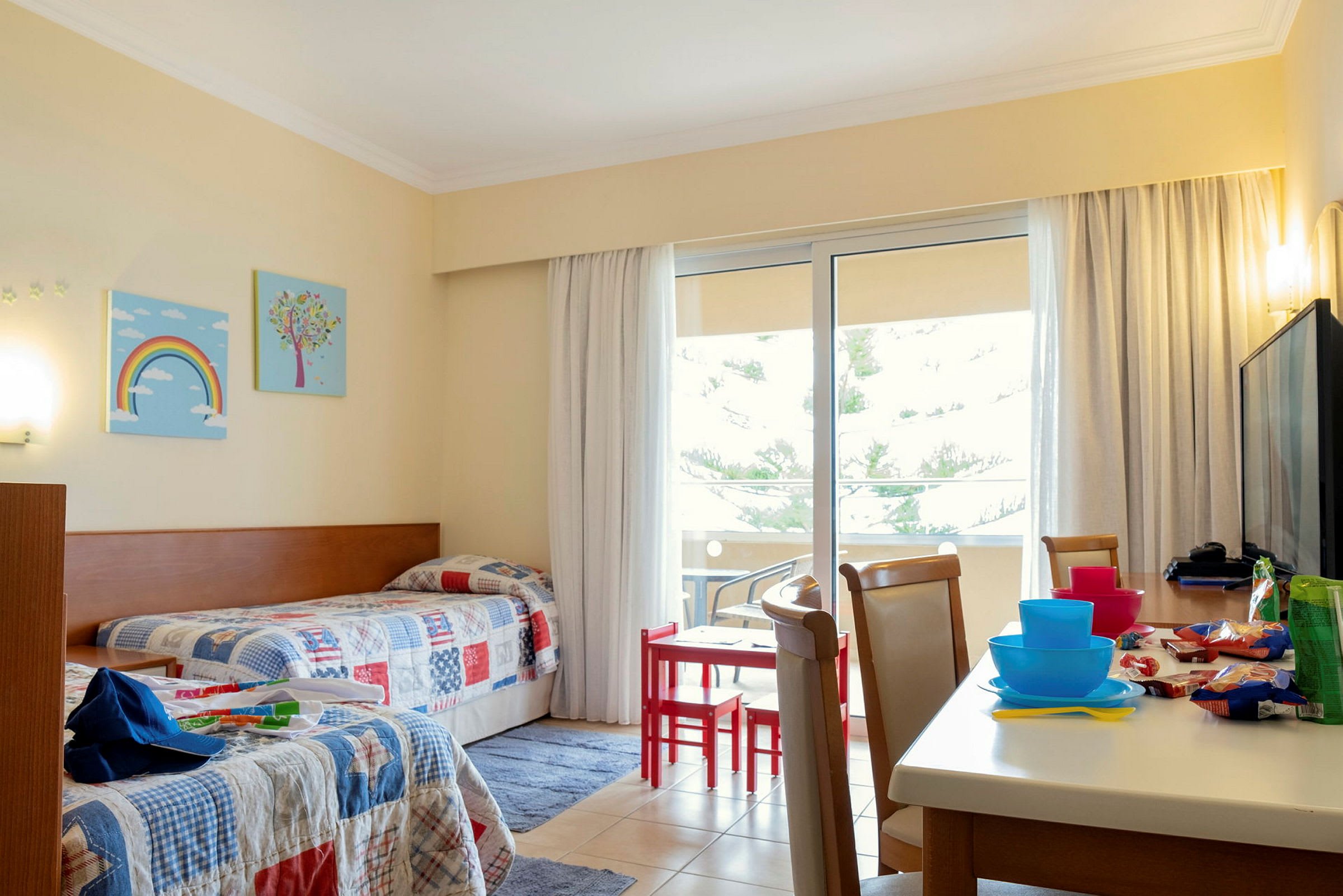 Hotellihuone, jossa kaksi yhden hengen vuodetta ja pöytä tuoleineen lähellä parveketta. (Tekoälyn luoma teksti)