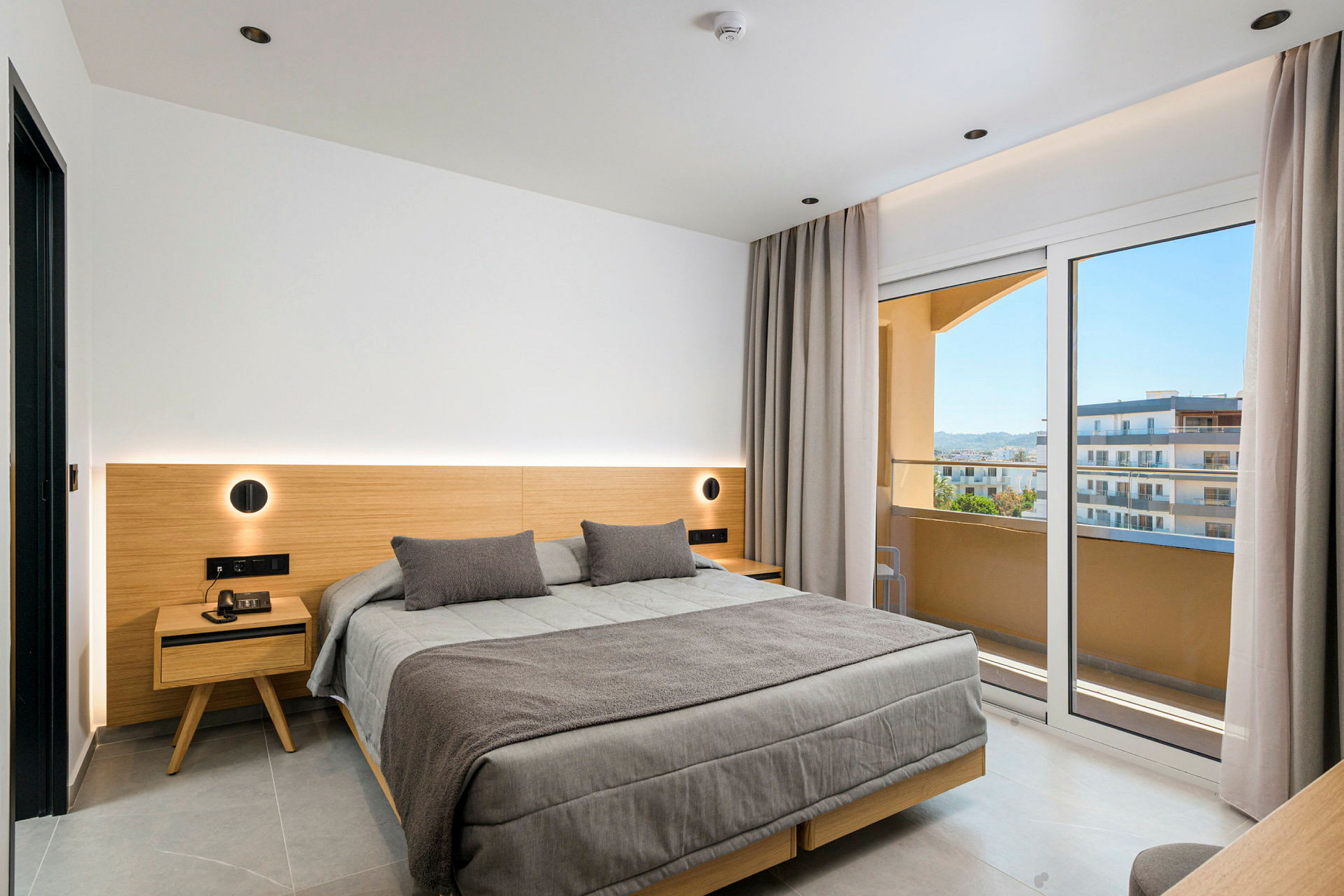 Moderni hotellihuone, jossa suuri sänky, puuyksityiskohtia ja lasiovet parvekkeelle näkymällä. (Tekoälyn luoma teksti)