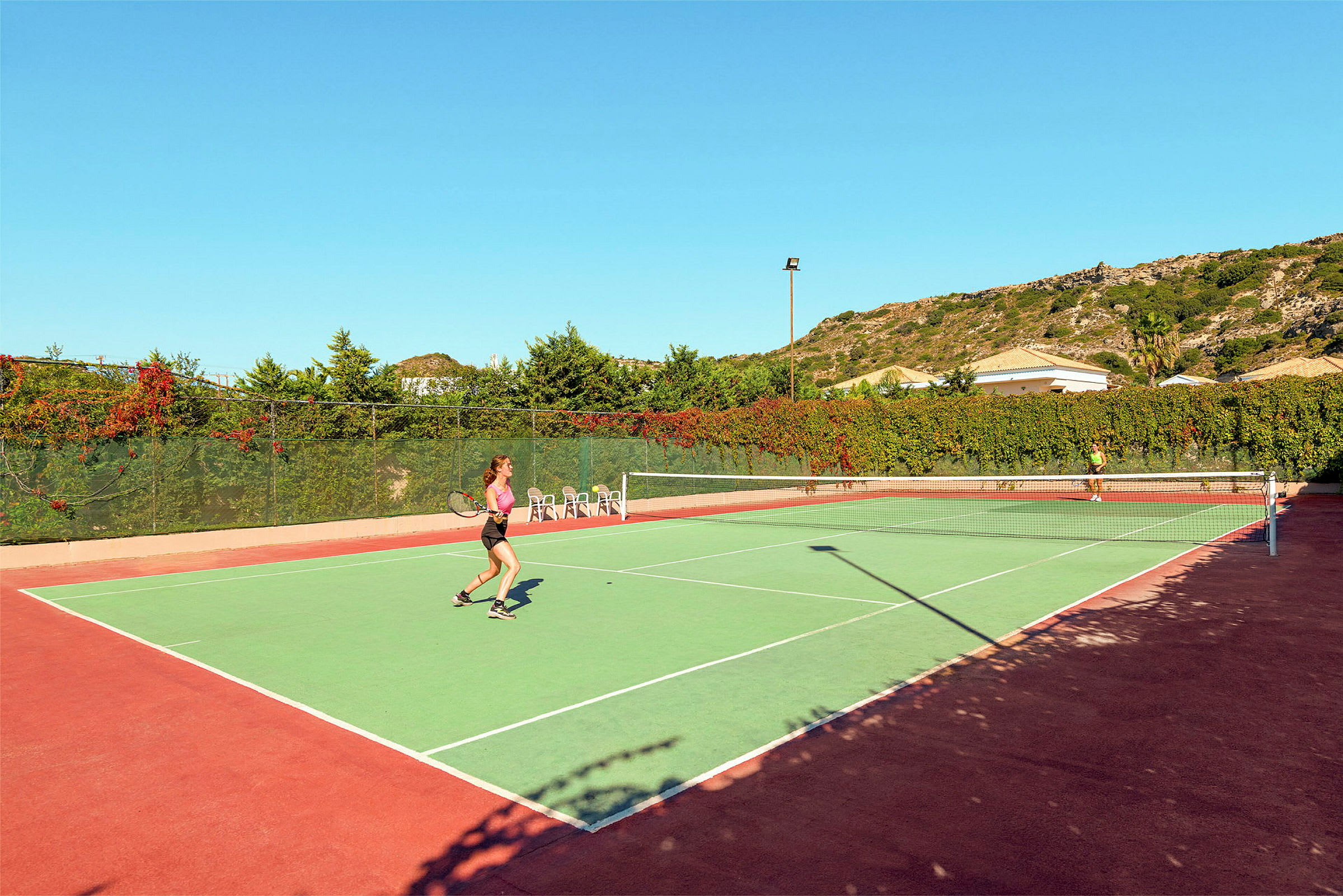 Kaksi henkilöä pelaa tennistä ulkokentällä kirkkaan taivaan alla. (Tekoälyn luoma teksti)