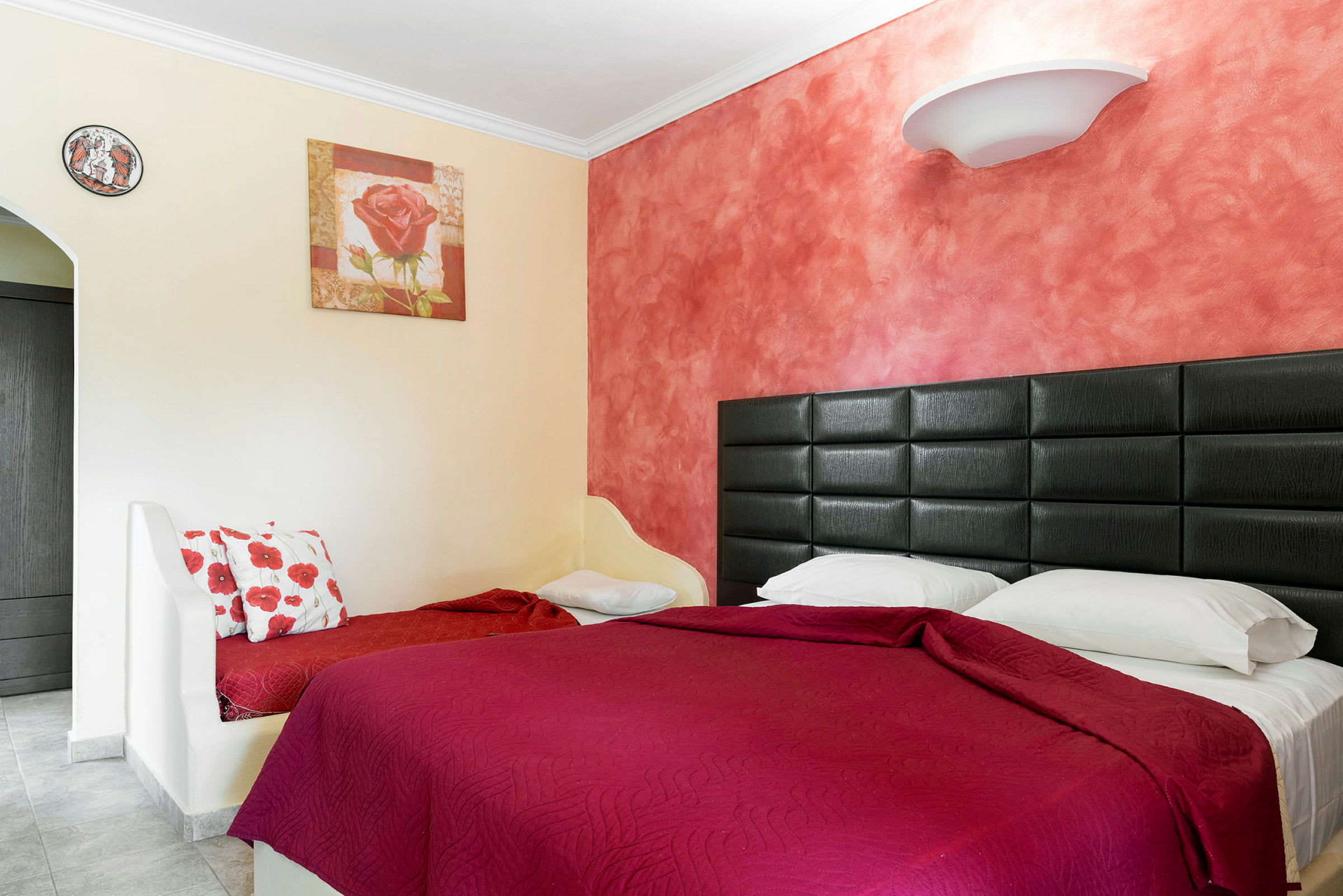 Hotellihuone, jossa on punaisilla vuodevaatteilla varustettu sänky ja taulu seinällä. (Tekoälyn luoma teksti)