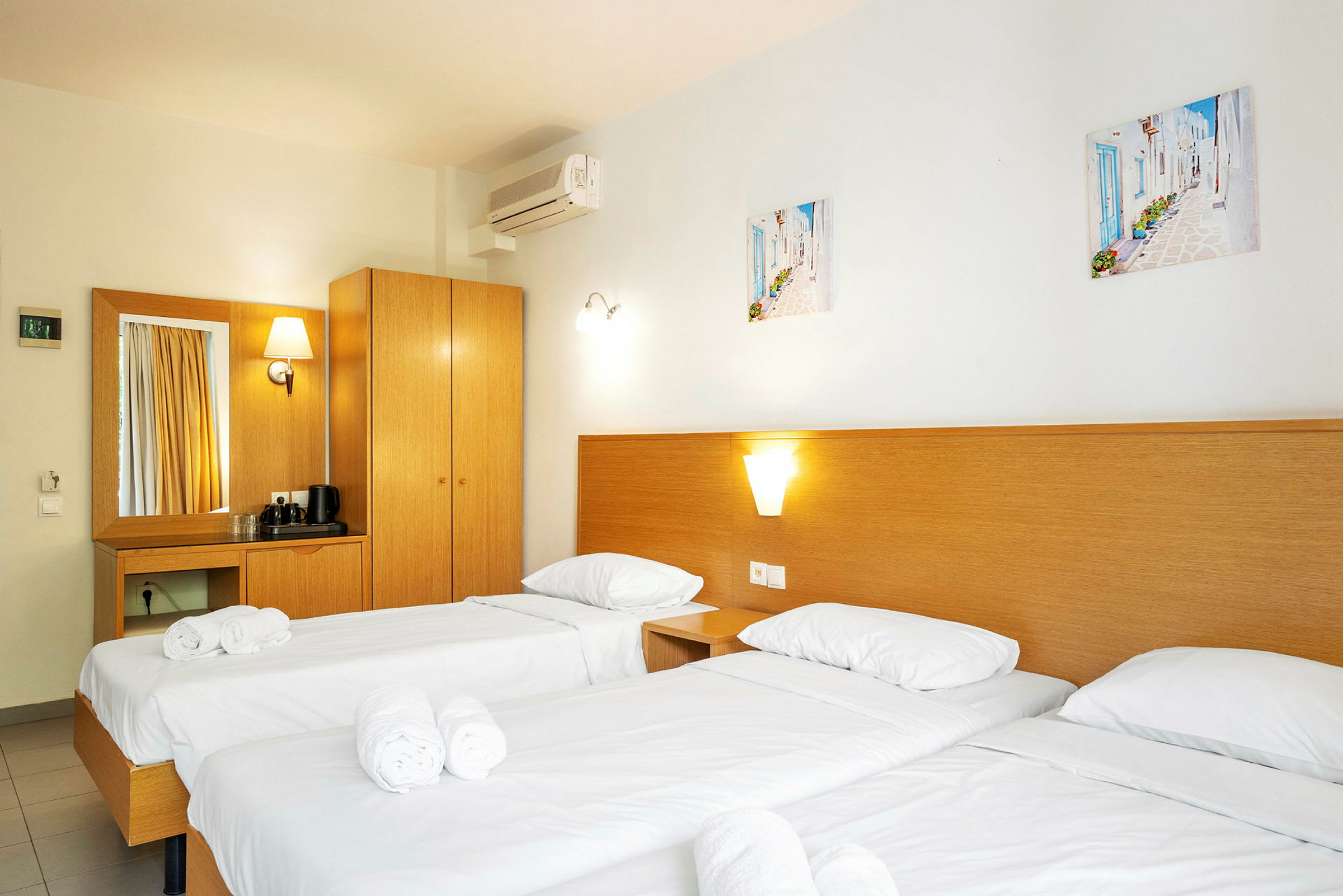 Hotellihuone, jossa on kolme erillistä vuodetta, valkoiset vuodevaatteet ja rullattuina pyyhkeet. (Tekoälyn luoma teksti)