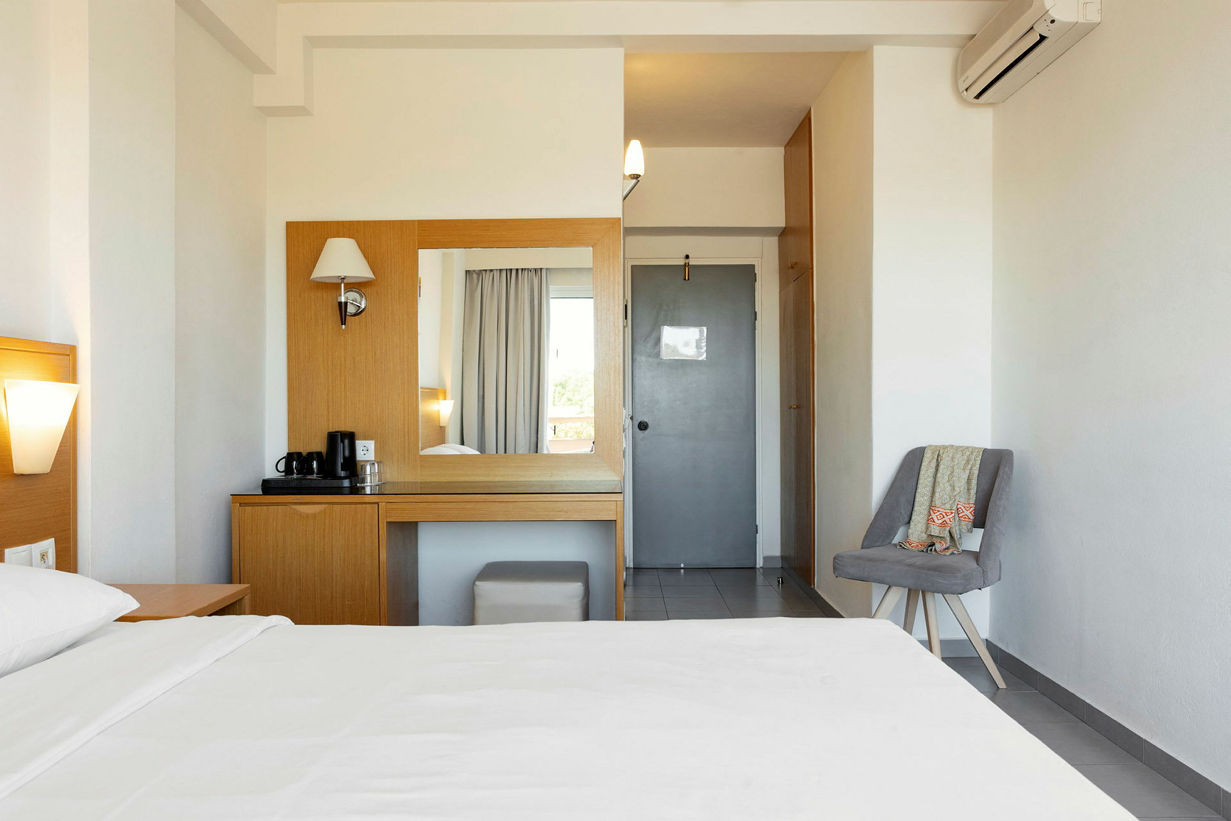Hotellihuone, jossa on sänky, pöytä ja peili, lisäksi tuoli sivulla. (Tekoälyn luoma teksti)