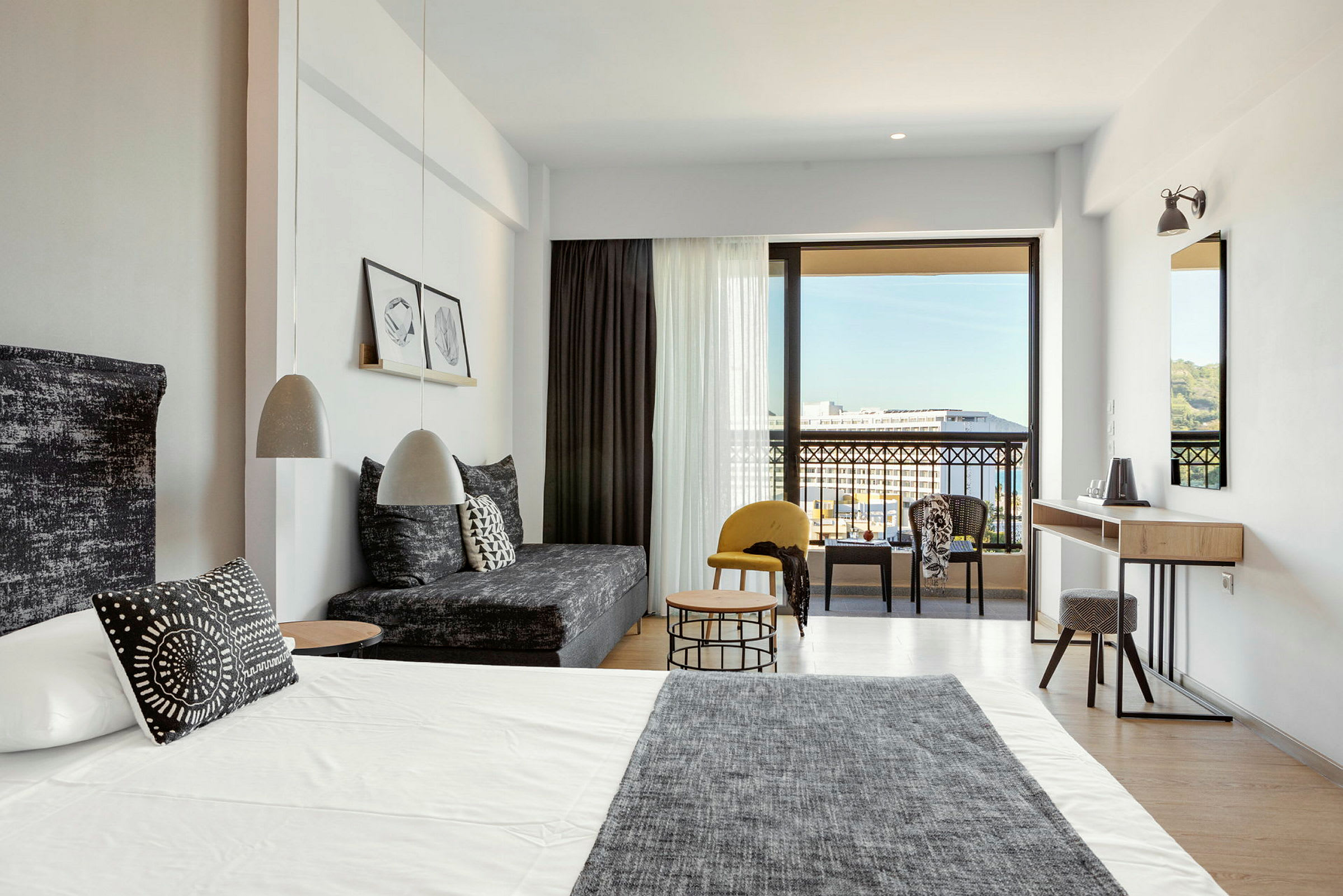 Moderni hotellihuone, jossa sänky, sohva ja istuinryhmä sekä näkymä parvekkeelle ja ympäristöön. (Tekoälyn luoma teksti)