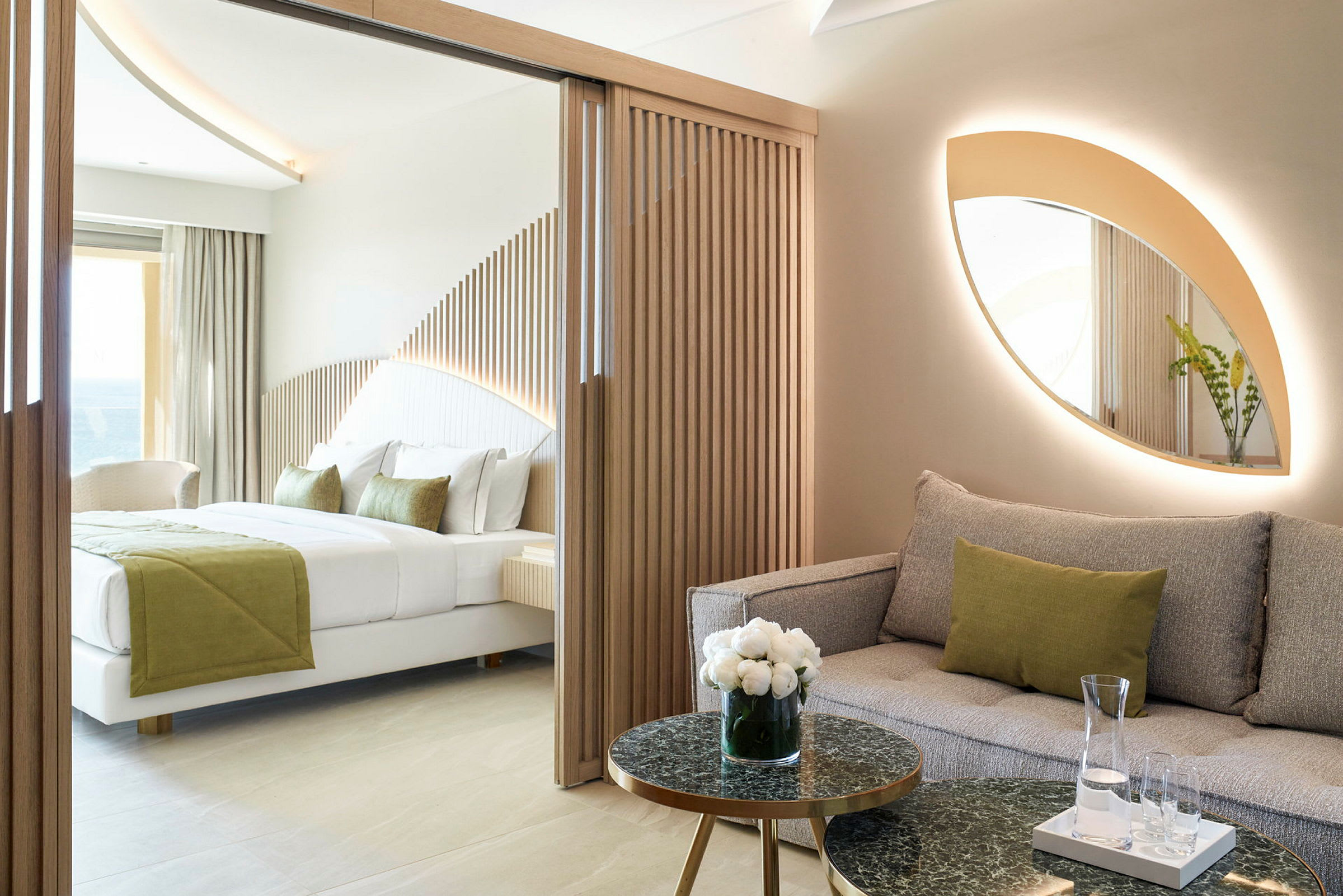 Moderni hotellihuone, jossa on sohva ja sänky, sisustettu luonnollisilla väreillä ja puuyksityiskohdilla. (Tekoälyn luoma teksti)