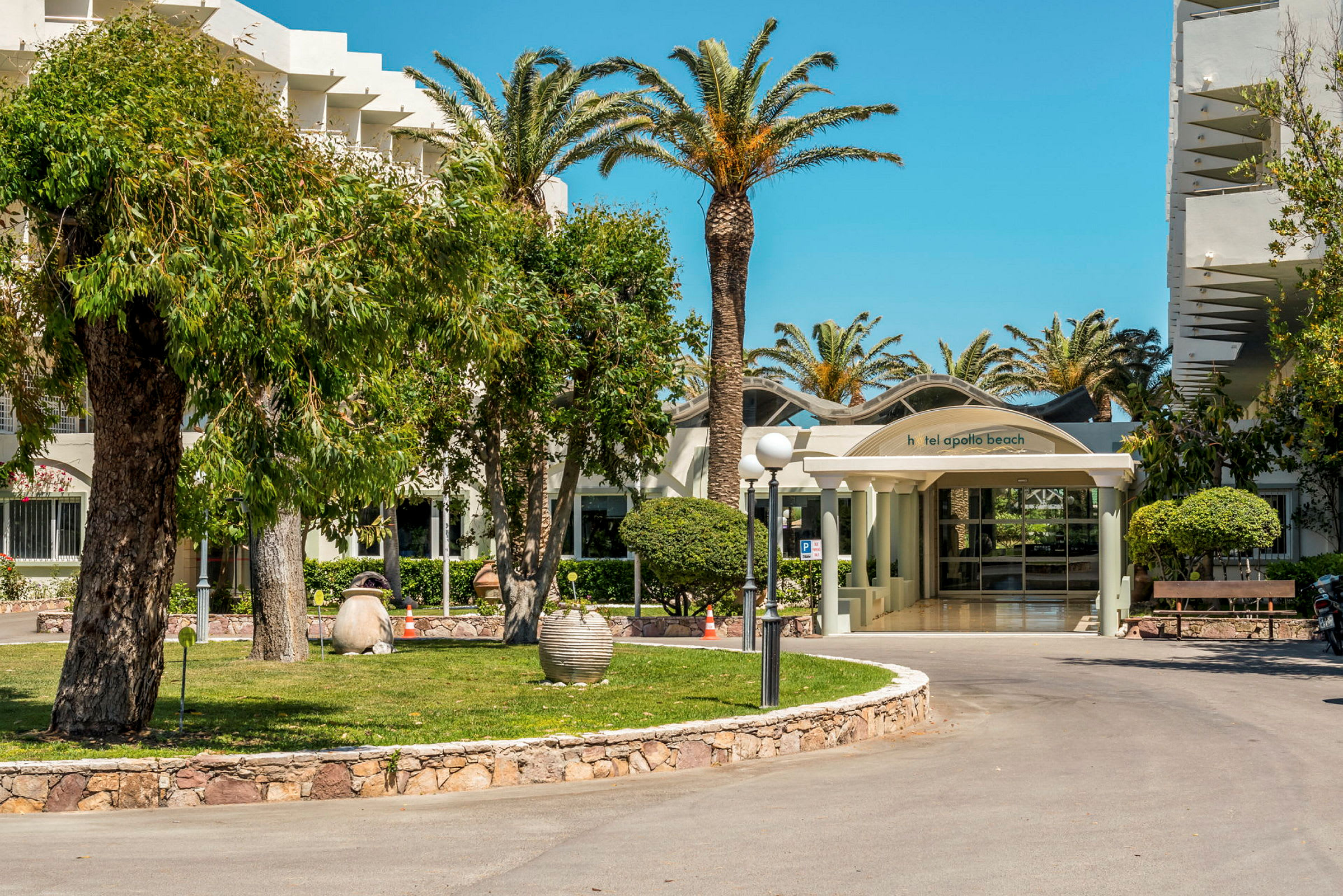 Hotel Apollo Beachin sisäänkäynti, jota ympäröivät palmut ja vehreys. (Tekoälyn luoma teksti)
