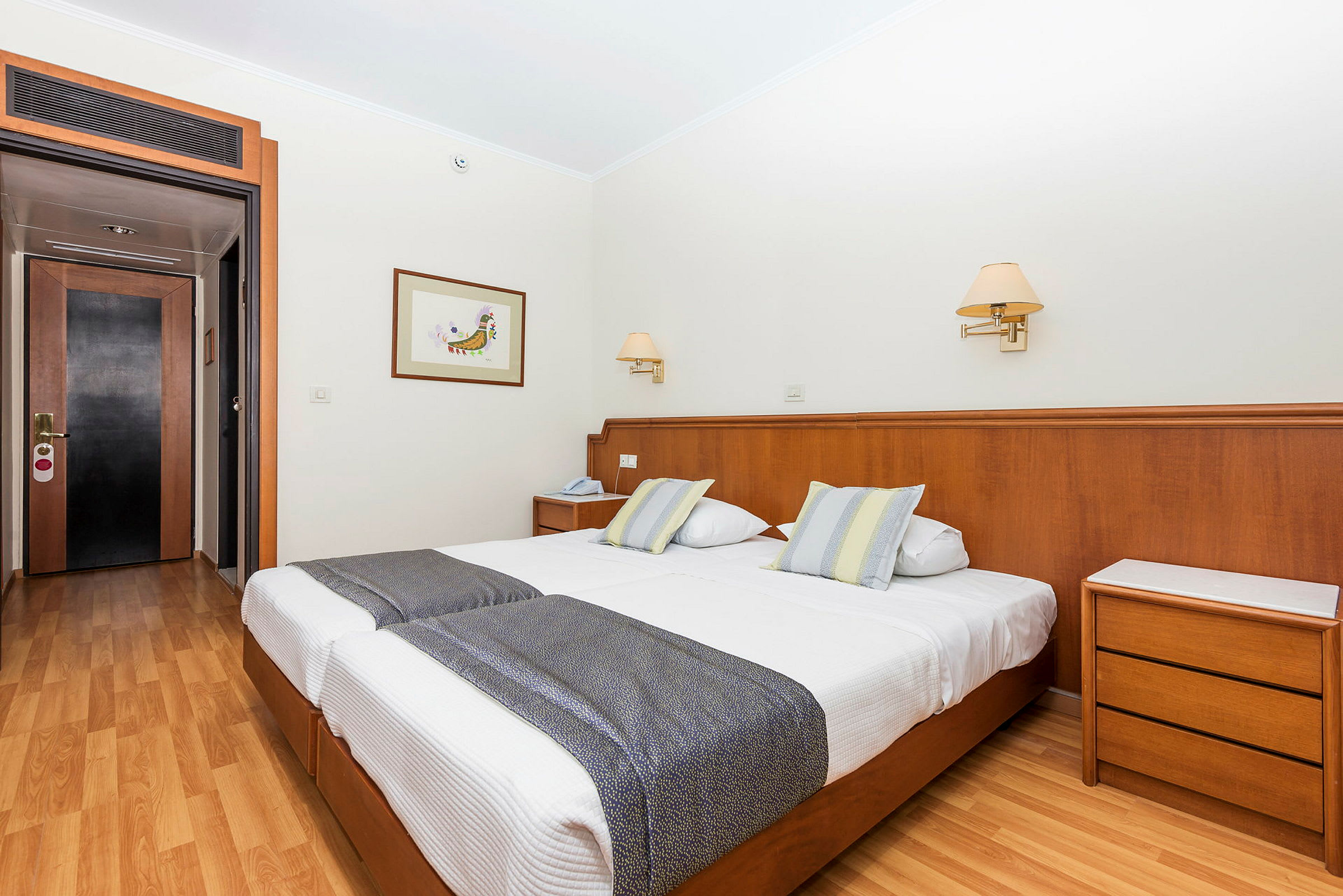 Hotellihuone, jossa kaksi erillisvuodetta, puulattia ja taustalla ovi. (Tekoälyn luoma teksti)