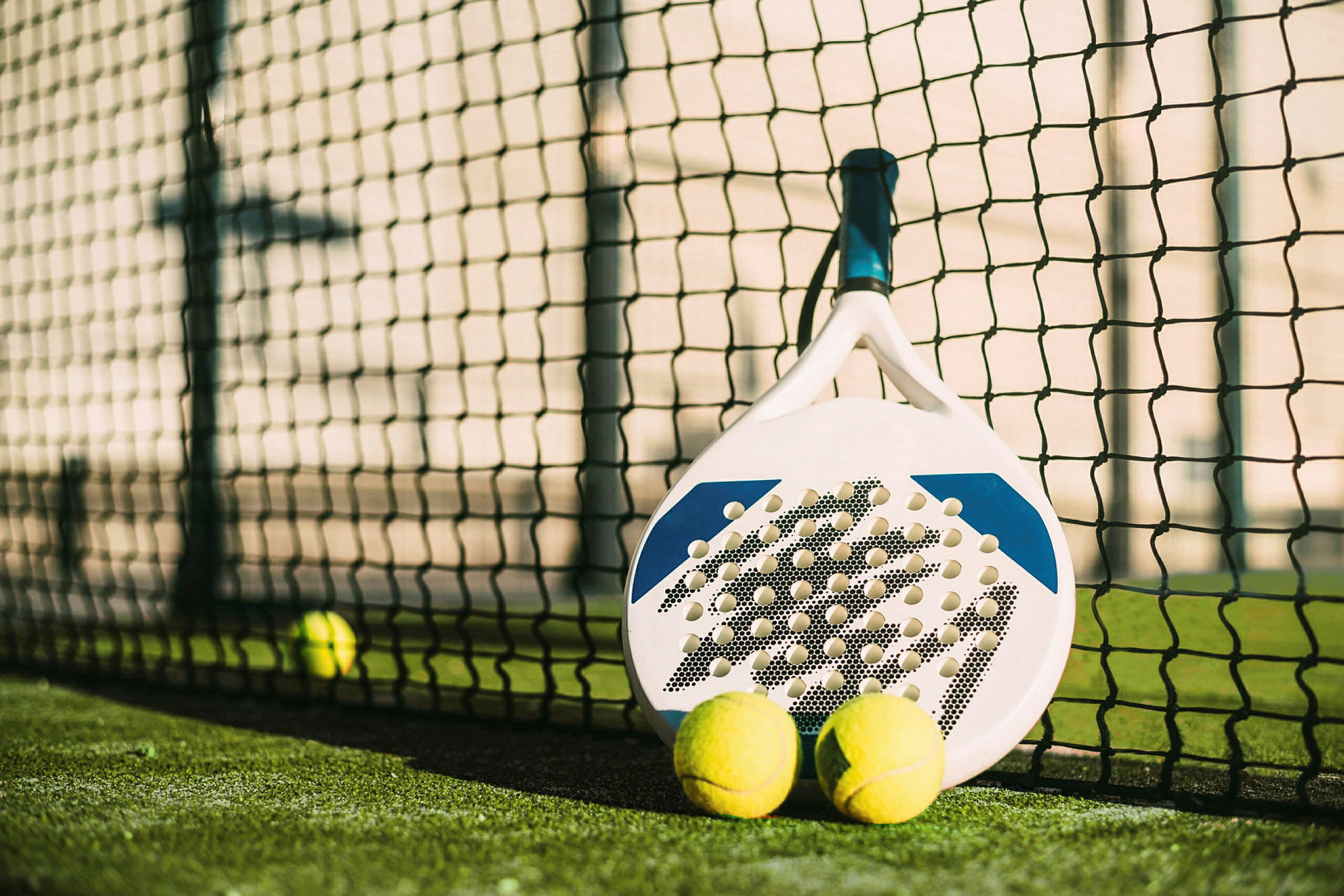 Padelmaila ja kaksi palloa verkon vieressä padelkentällä. (Tekoälyn luoma teksti)