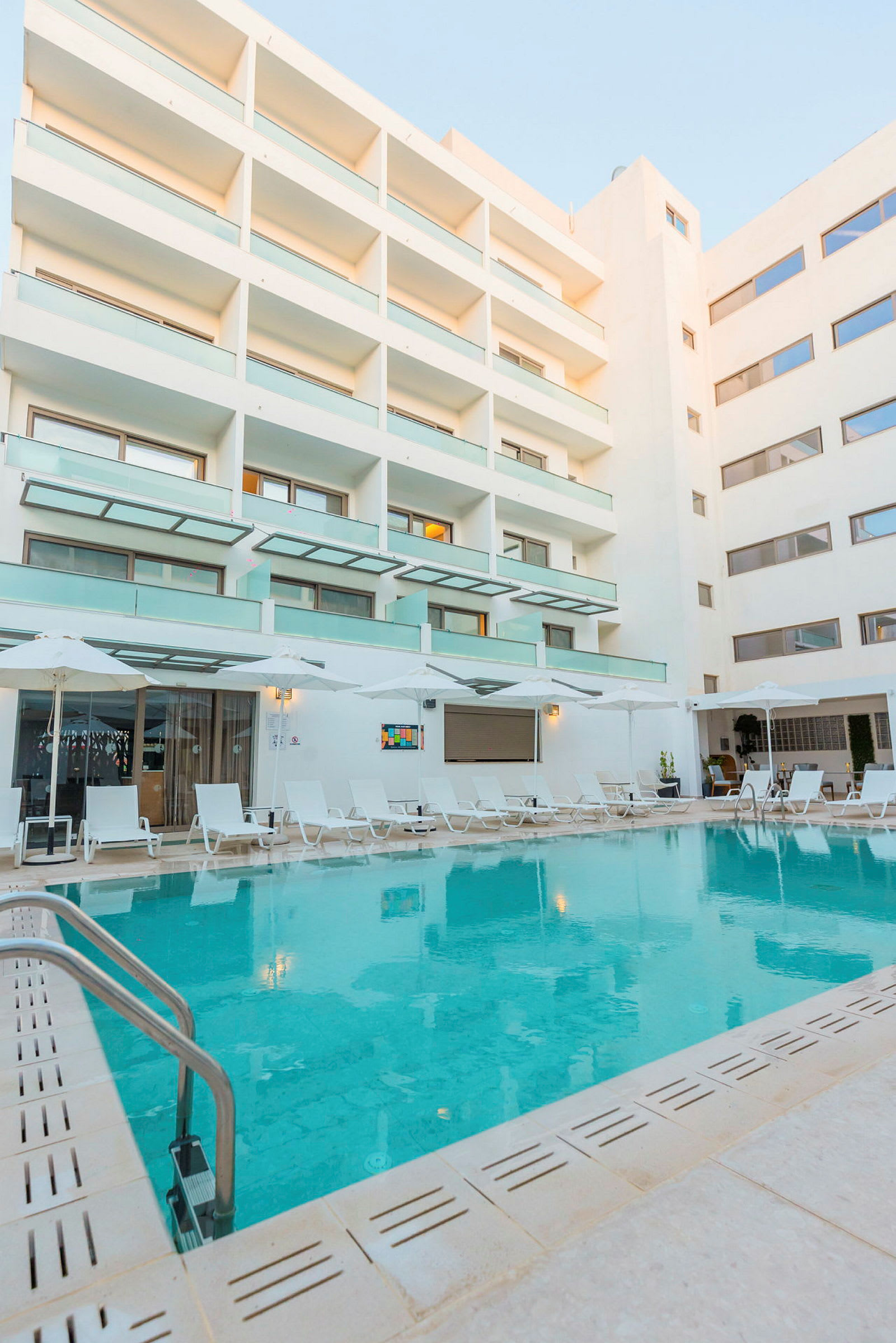 Hotellin uima-allas, jonka ympärillä on aurinkotuoleja ja nykyaikainen hotellirakennus. (Tekoälyn luoma teksti)