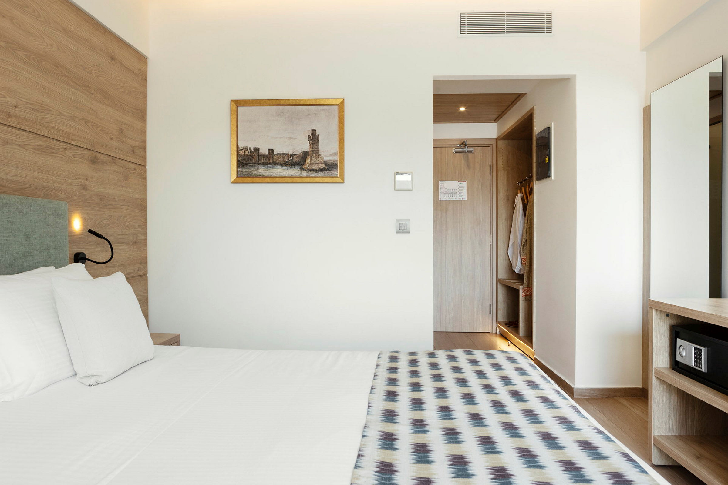 Hotellihuone, jossa on sänky, seinämaalaus ja avoin vaatekaappi. (Tekoälyn luoma teksti)