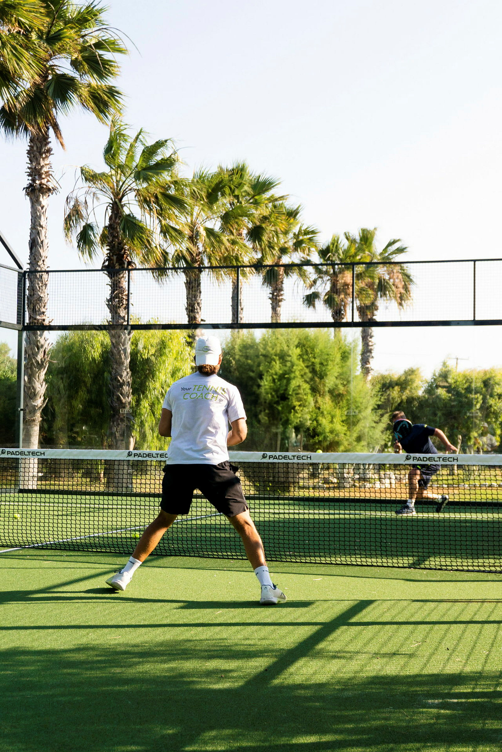 Mies pelaa padeltennistä ulkokentällä palmujen ympäröimänä. (Tekoälyn luoma teksti)