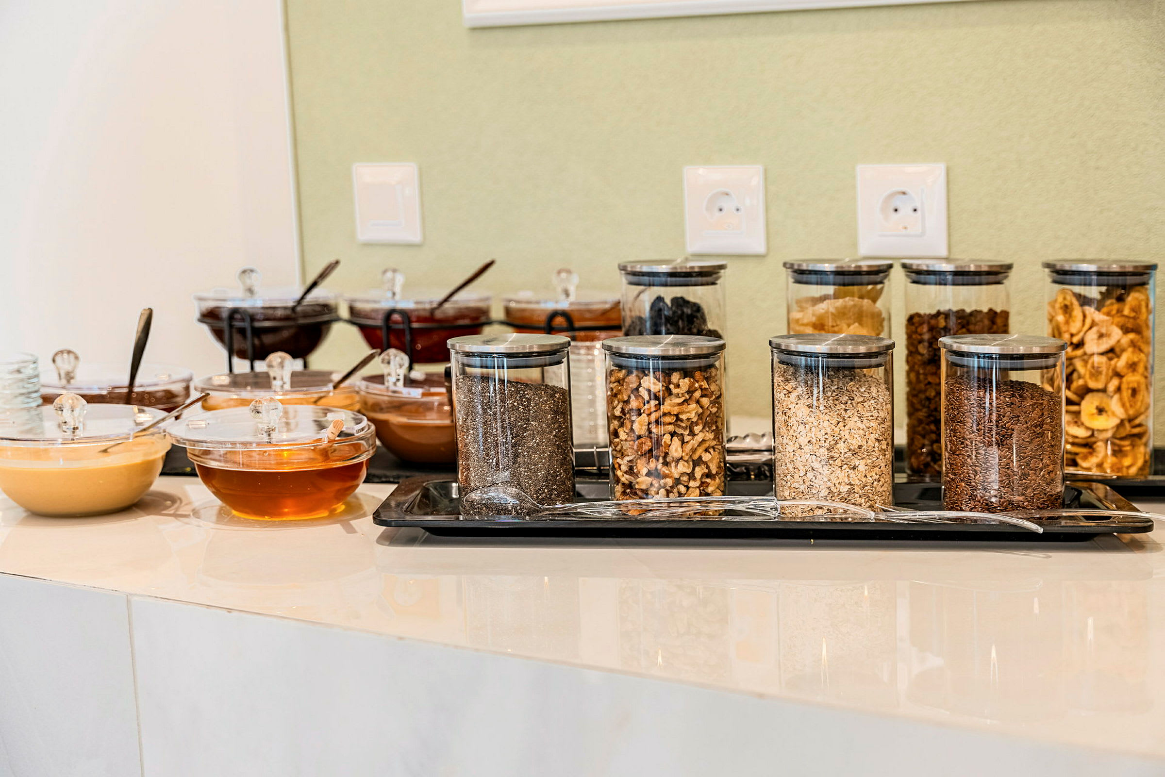 Buffet, joka sisältää erilaisia pähkinöitä, siemeniä ja hunajaa lasipurkeissa. (Tekoälyn luoma teksti)