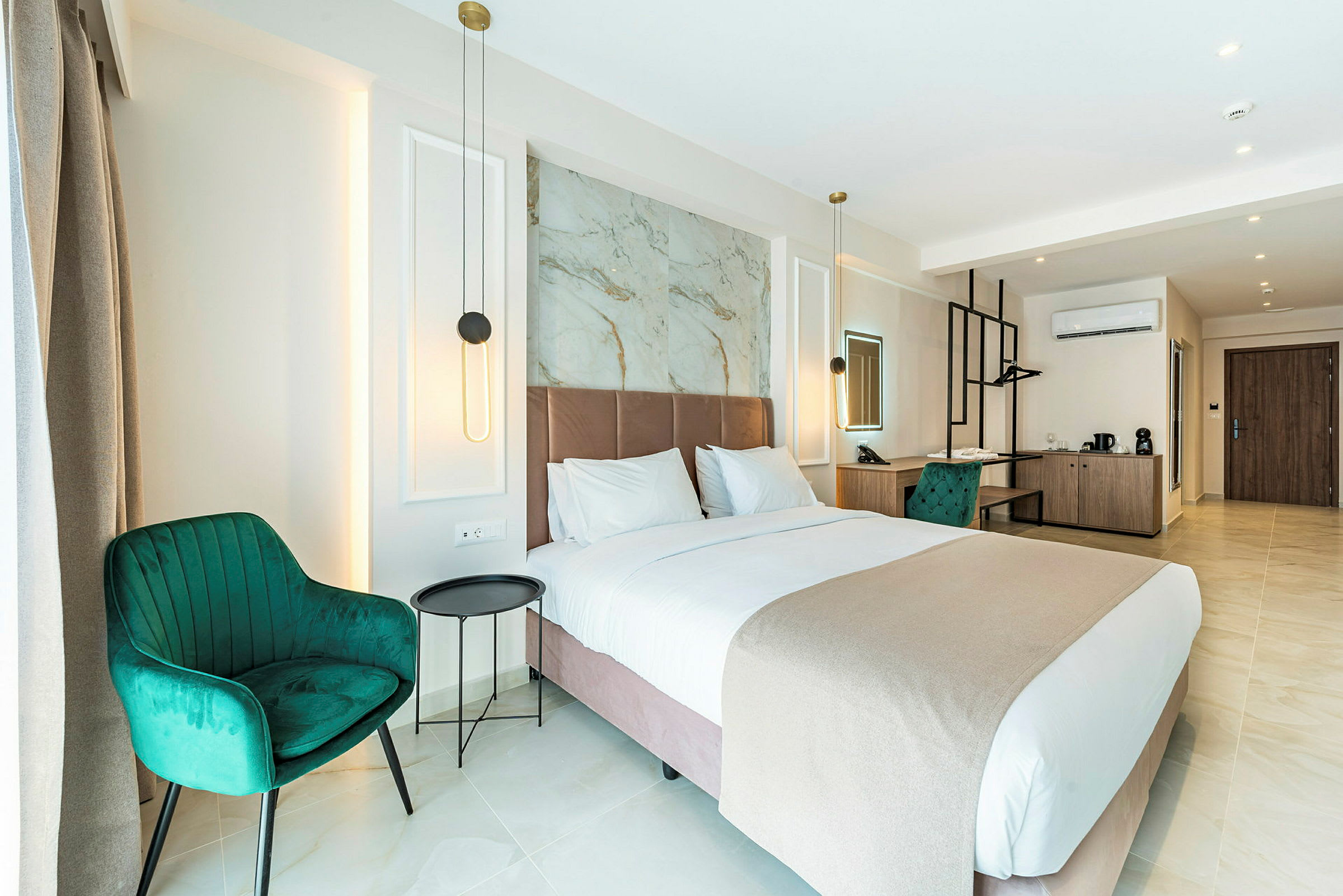 Moderni hotellihuone, jossa on iso sänky, vihreät tuolit ja kirjoituspöytä. Huone on hyvin valaistu seinävalaisimilla ja sisustettu tyylikkäästi. (Tekoälyn luoma teksti)