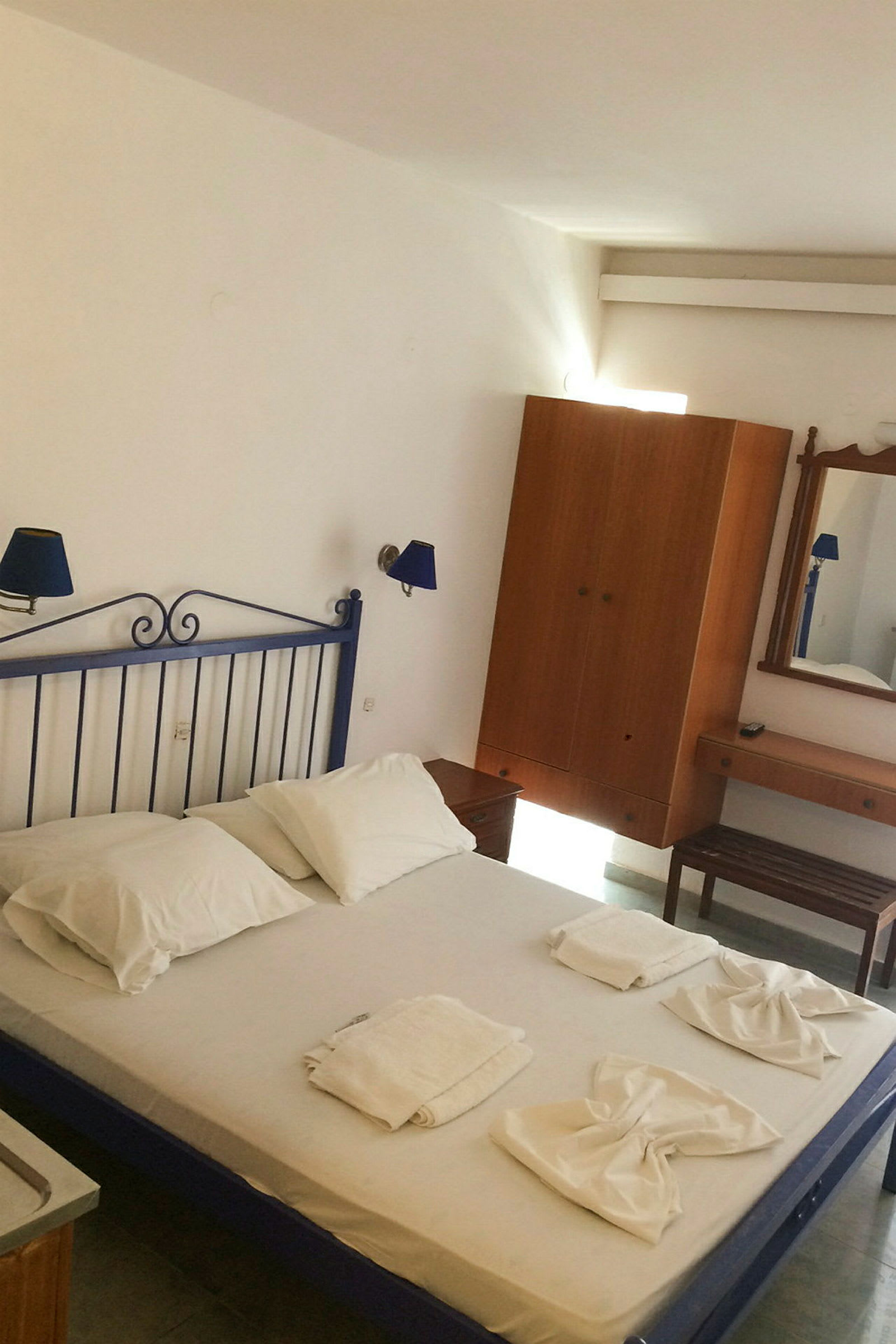 Hotellihuone, jossa vuode valkoisilla vuodevaatteilla, vuoteelle asetellut pyyhkeet ja huonekaluja kuten vaatekaappi ja peili. (Tekoälyn luoma teksti)