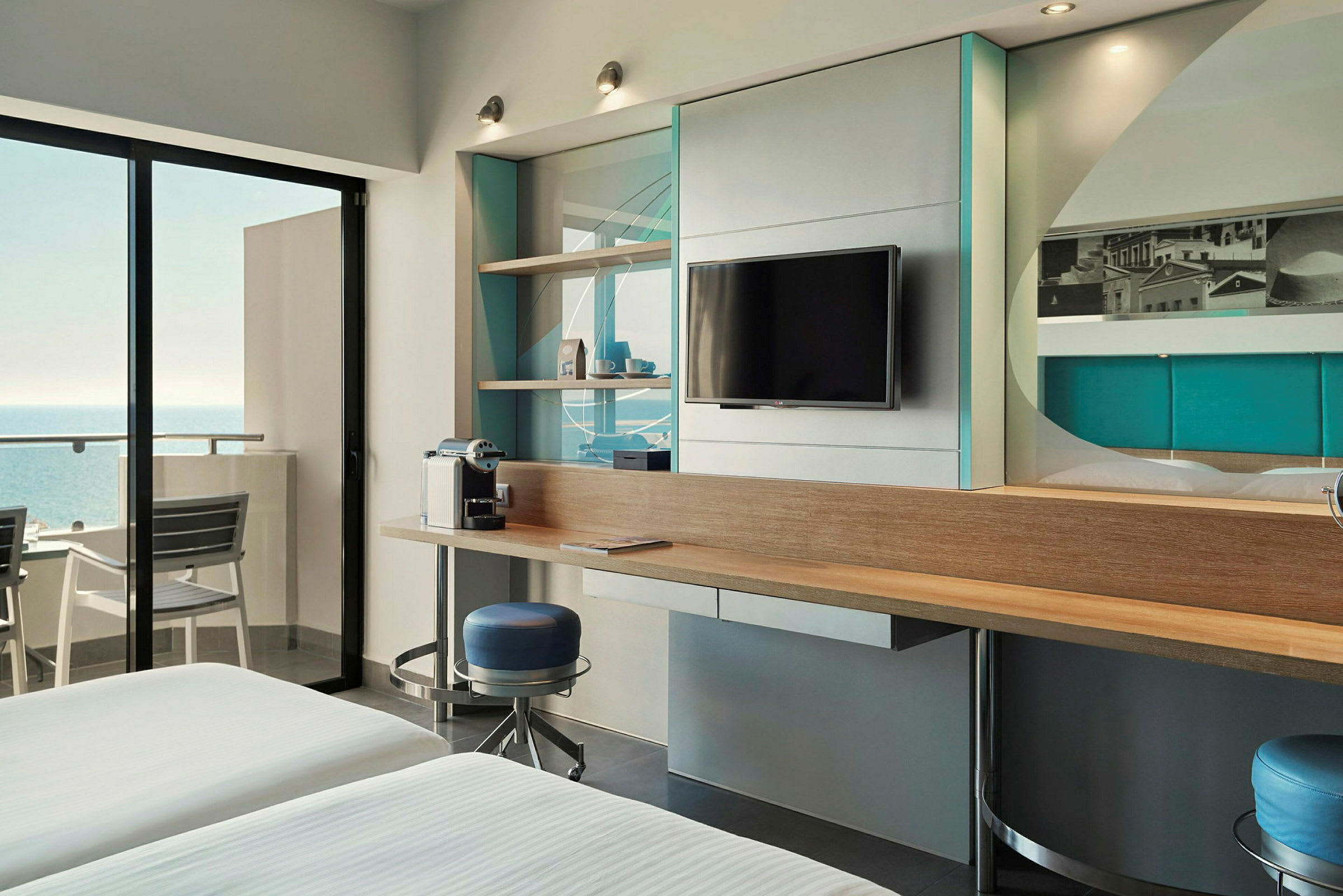 Moderni hotellihuone merinäköalalla, seinällä televisio ja kahvinkeitin työpöydällä. (Tekoälyn luoma teksti)