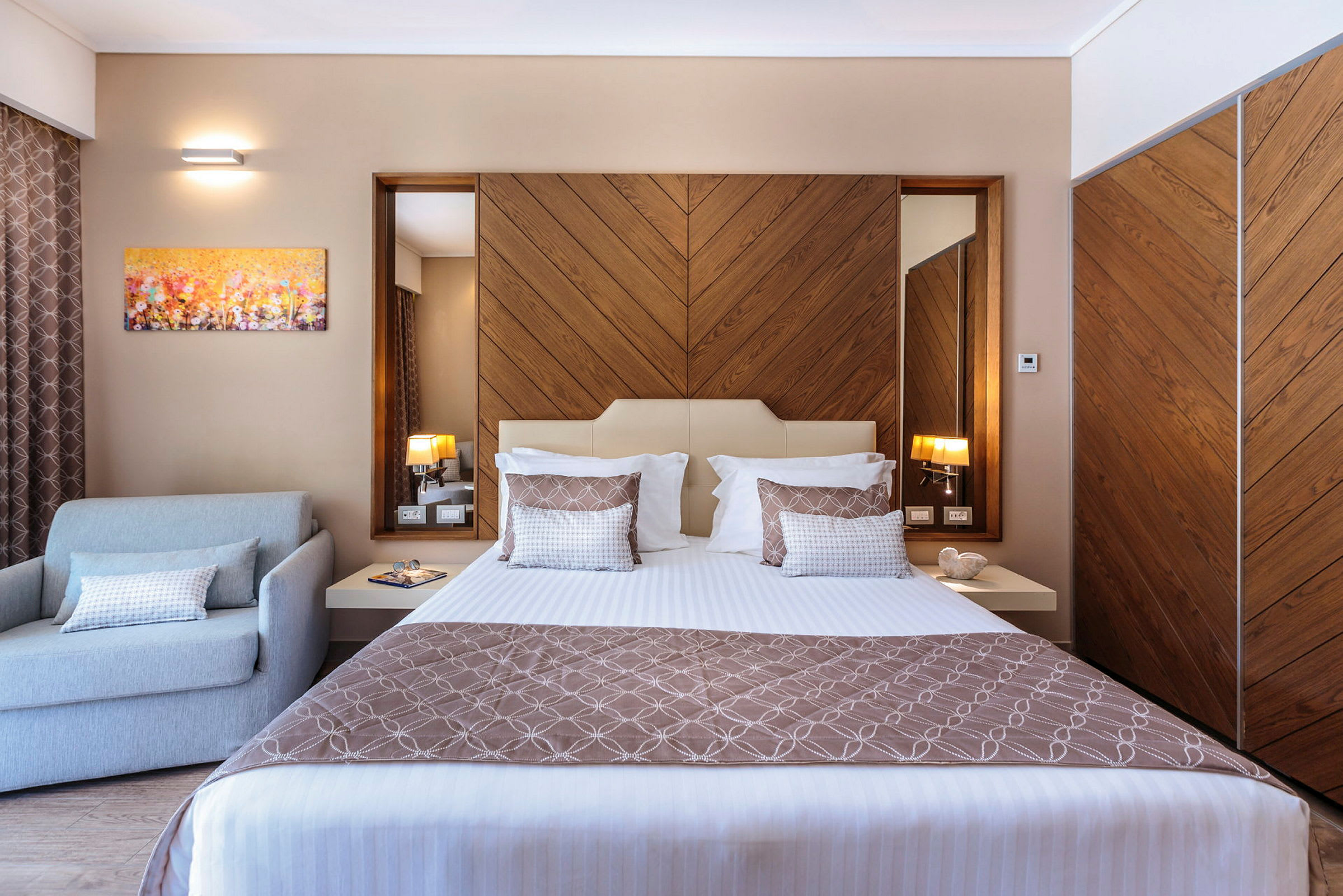 Moderni hotellihuone, jossa on sänky, nojatuoli ja puuyksityiskohtia sisustuksessa. (Tekoälyn luoma teksti)