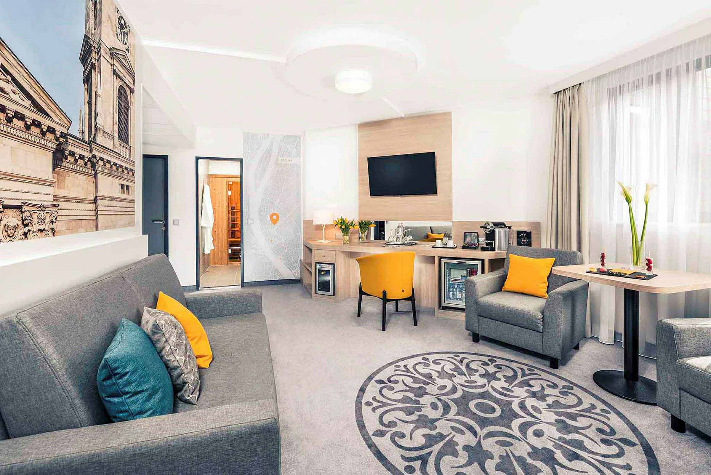 Hotellihuone, jossa oleskelutila, työpöytä ja suuri seinäkuva rakennuksen julkisivusta. (Tekoälyn luoma teksti)