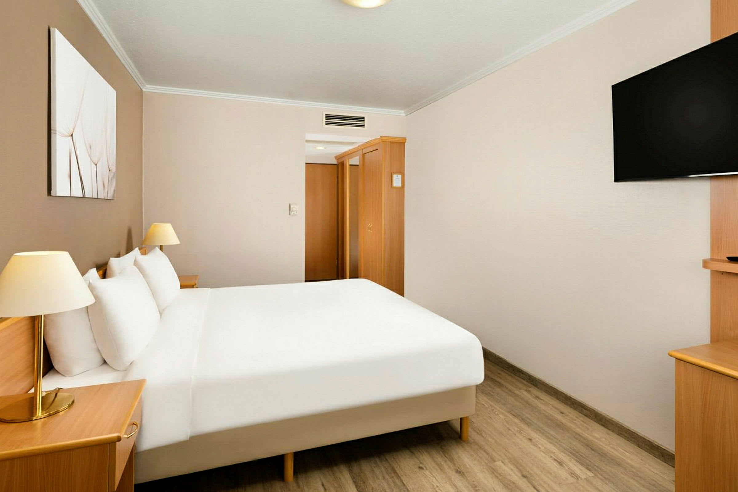 Hotellihuone, jossa on parivuode, valkoiset lakanat, yöpöydät lampuilla, seinälle kiinnitetty televisio ja puukalusteita. (Tekoälyn luoma teksti)