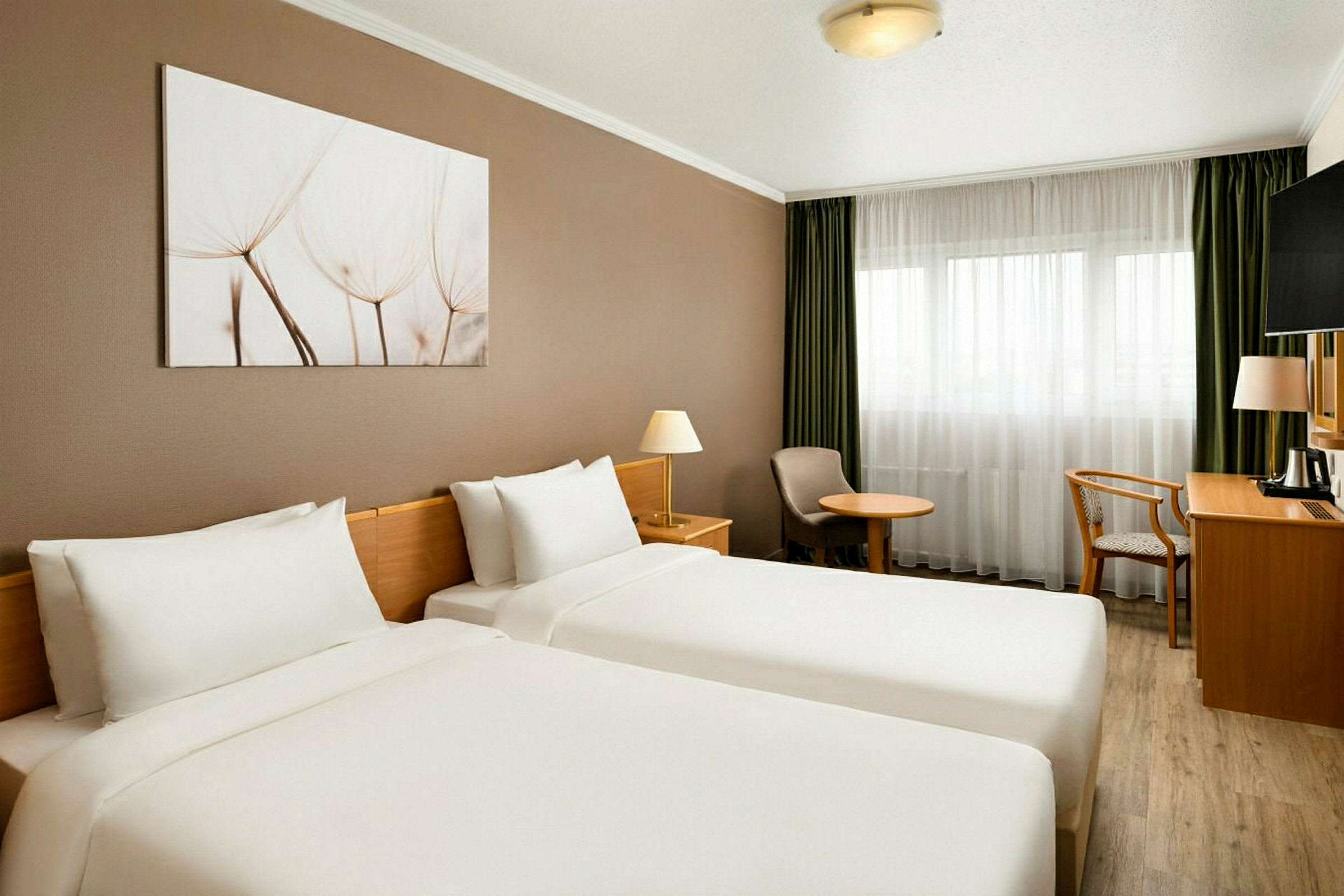 Hotellihuone, jossa kaksi yhden hengen vuodetta, valkoiset vuodevaatteet, seinällä maalaus sekä vihreät verhot ikkunassa. (Tekoälyn luoma teksti)