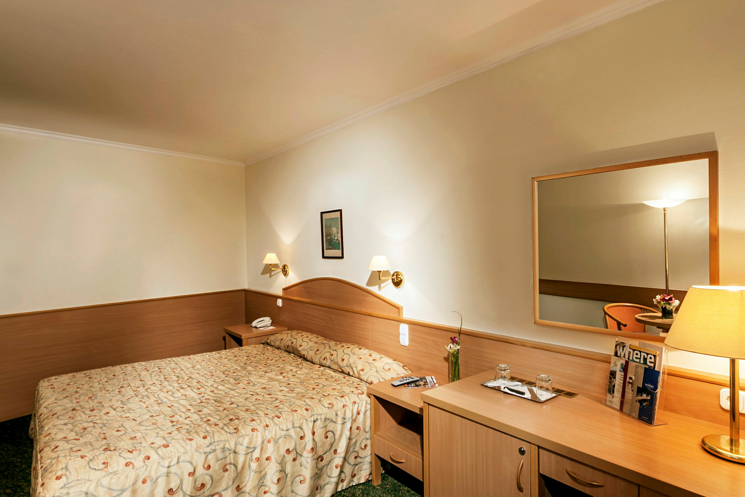 Hotellihuone, jossa on parisänky, yöpöytä, peili ja kirjoituspöytä. (Tekoälyn luoma teksti)