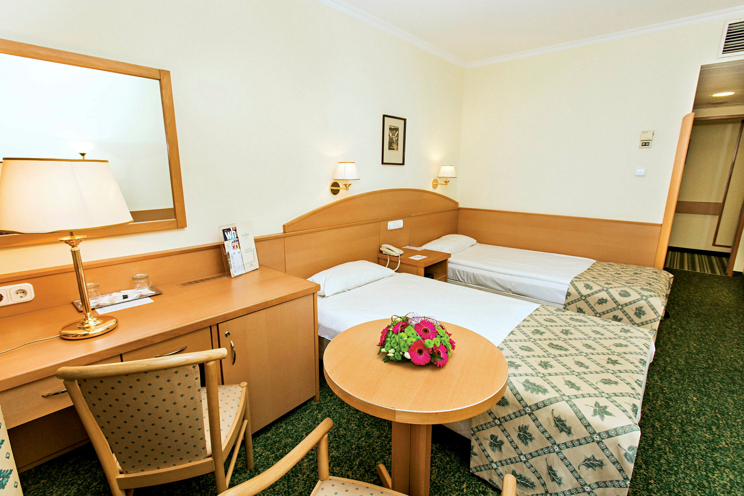 Kaksi erillistä sänkyä hotellihuoneessa, jossa on puukalusteet ja kukkia pöydällä. (Tekoälyn luoma teksti)