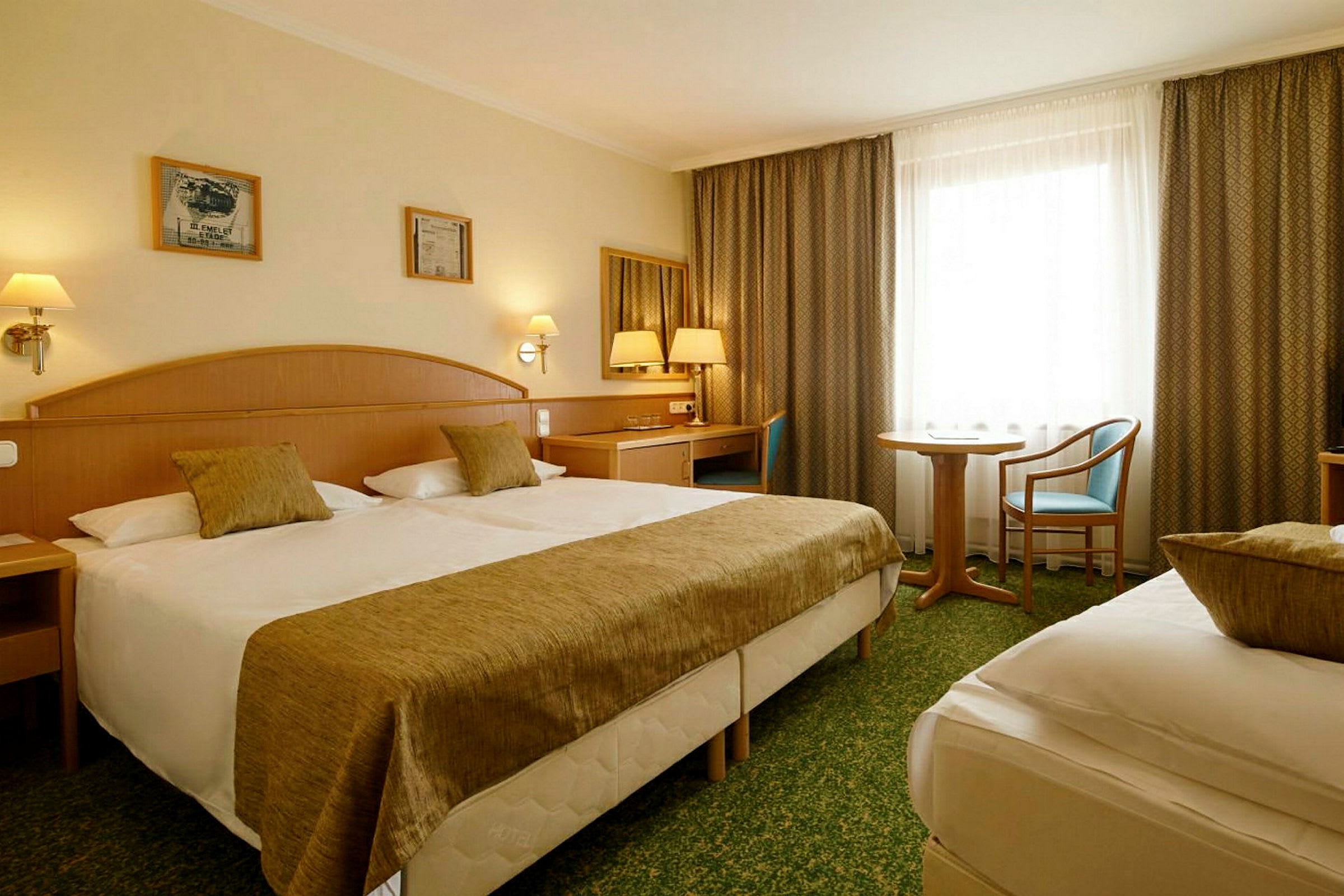 Hotellihuone, jossa on kaksi sänkyä, kirjoituspöytä ja istuinryhmä. (Tekoälyn luoma teksti)