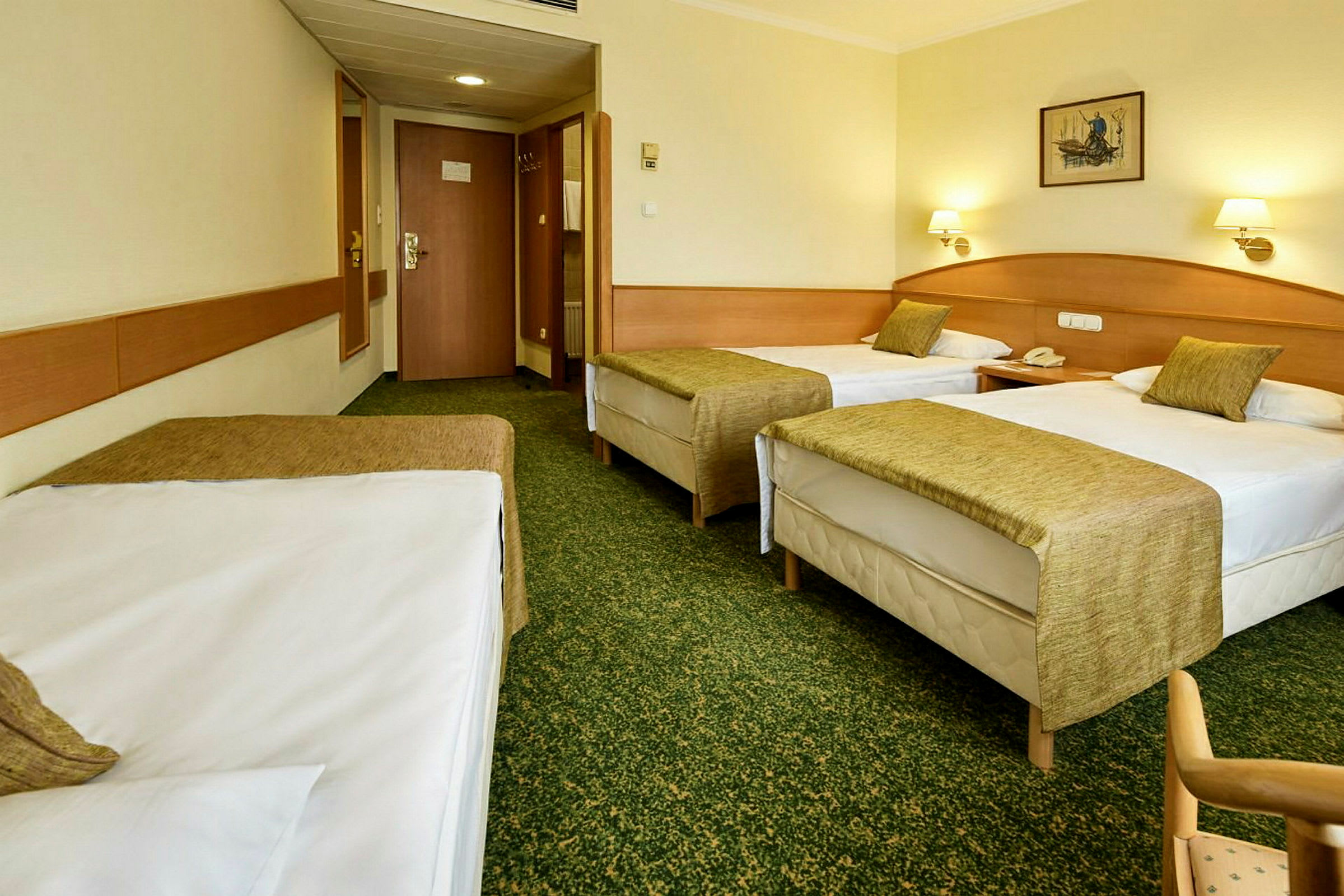 Hotellihuone, jossa on kolme erillistä vuodetta, vihreät päiväpeitot ja vaaleat seinät. (Tekoälyn luoma teksti)