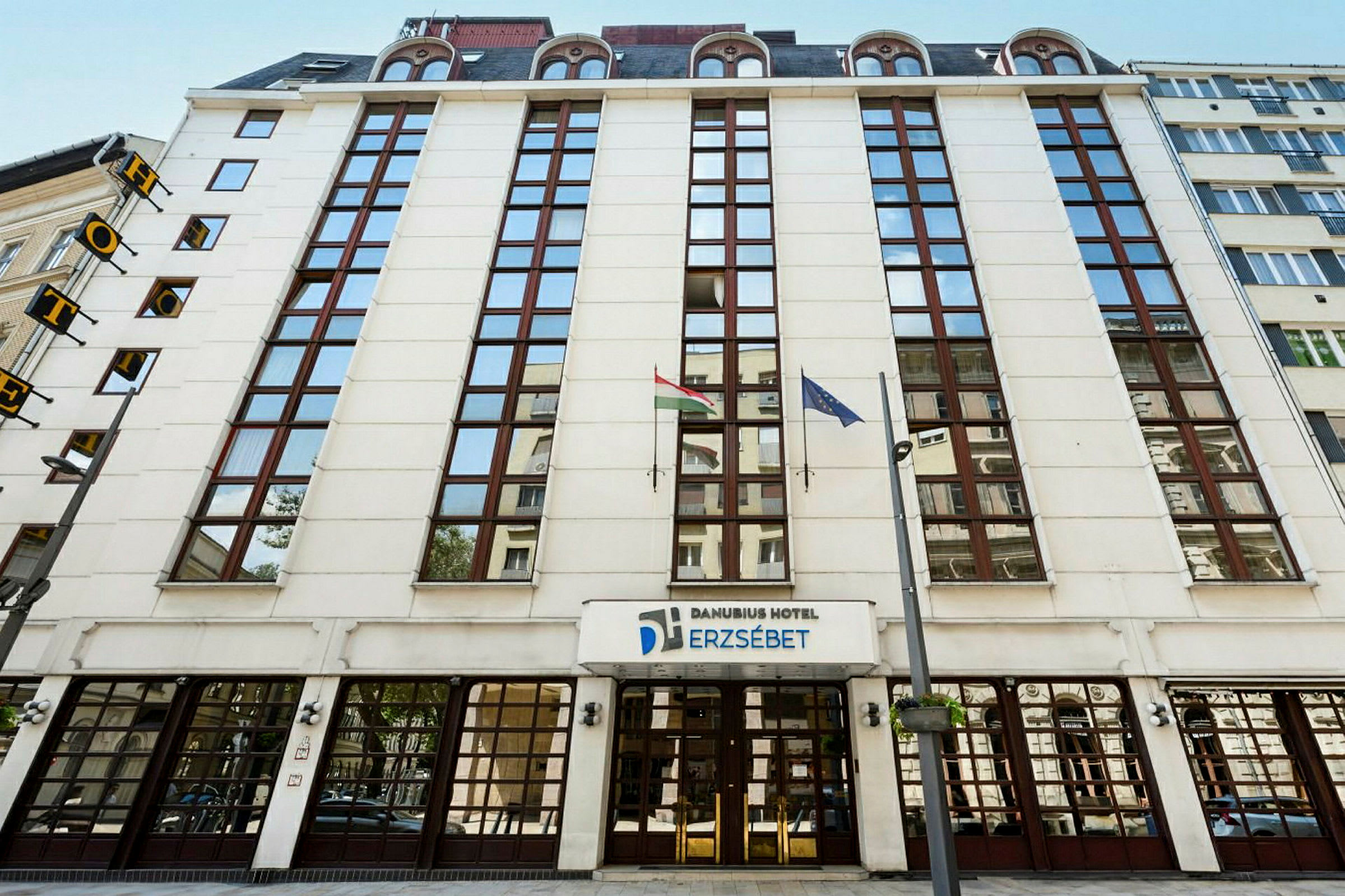 Danubius Hotel Erzsébetin etupuoli lasi-ikkunoilla ja lipuilla. (Tekoälyn luoma teksti)