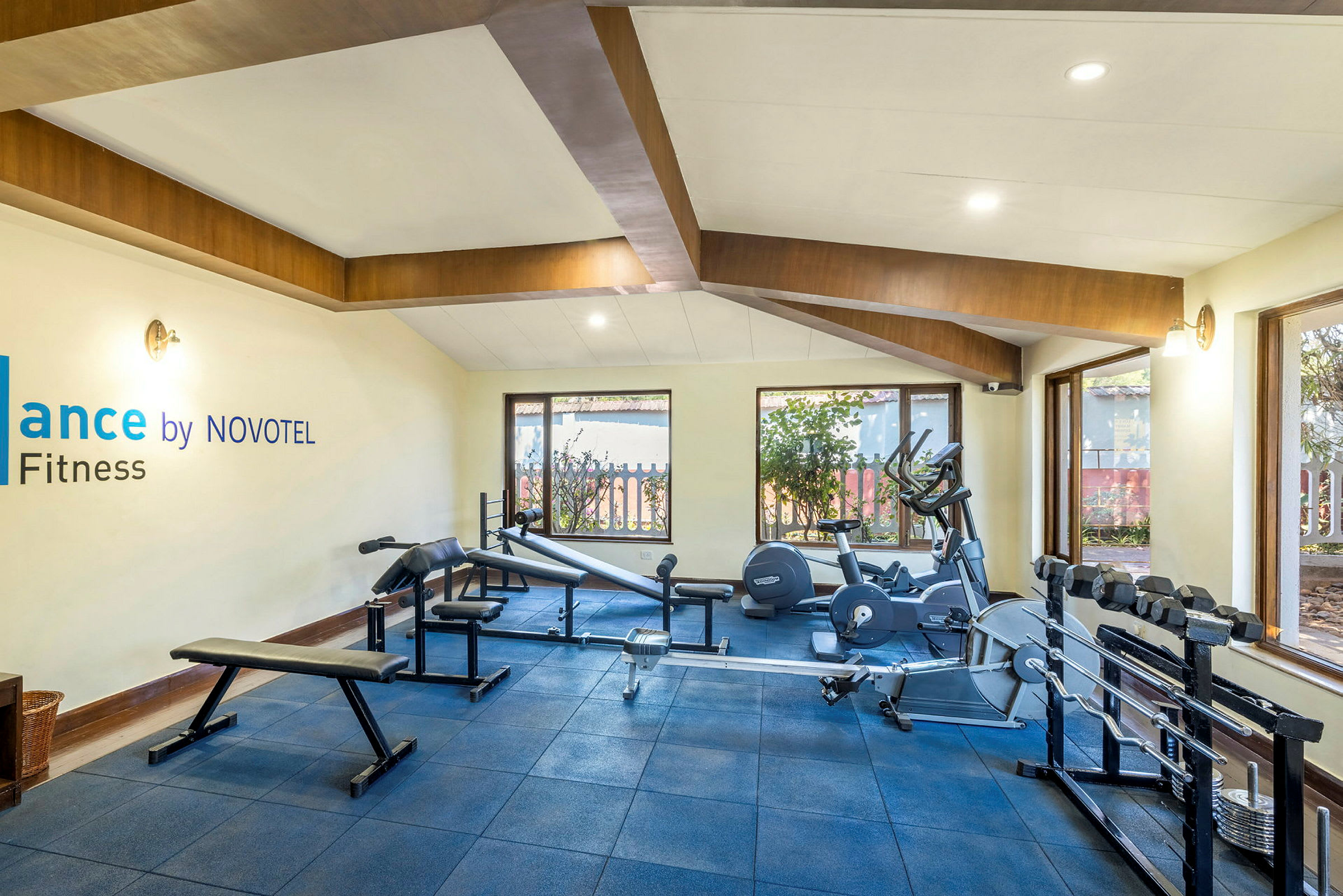 Kuntosali, jossa kuntoiluvälineitä, ikkunoita ja kyltti, jossa lukee 'Balance by NOVOTEL Fitness'. (Tekoälyn luoma teksti)
