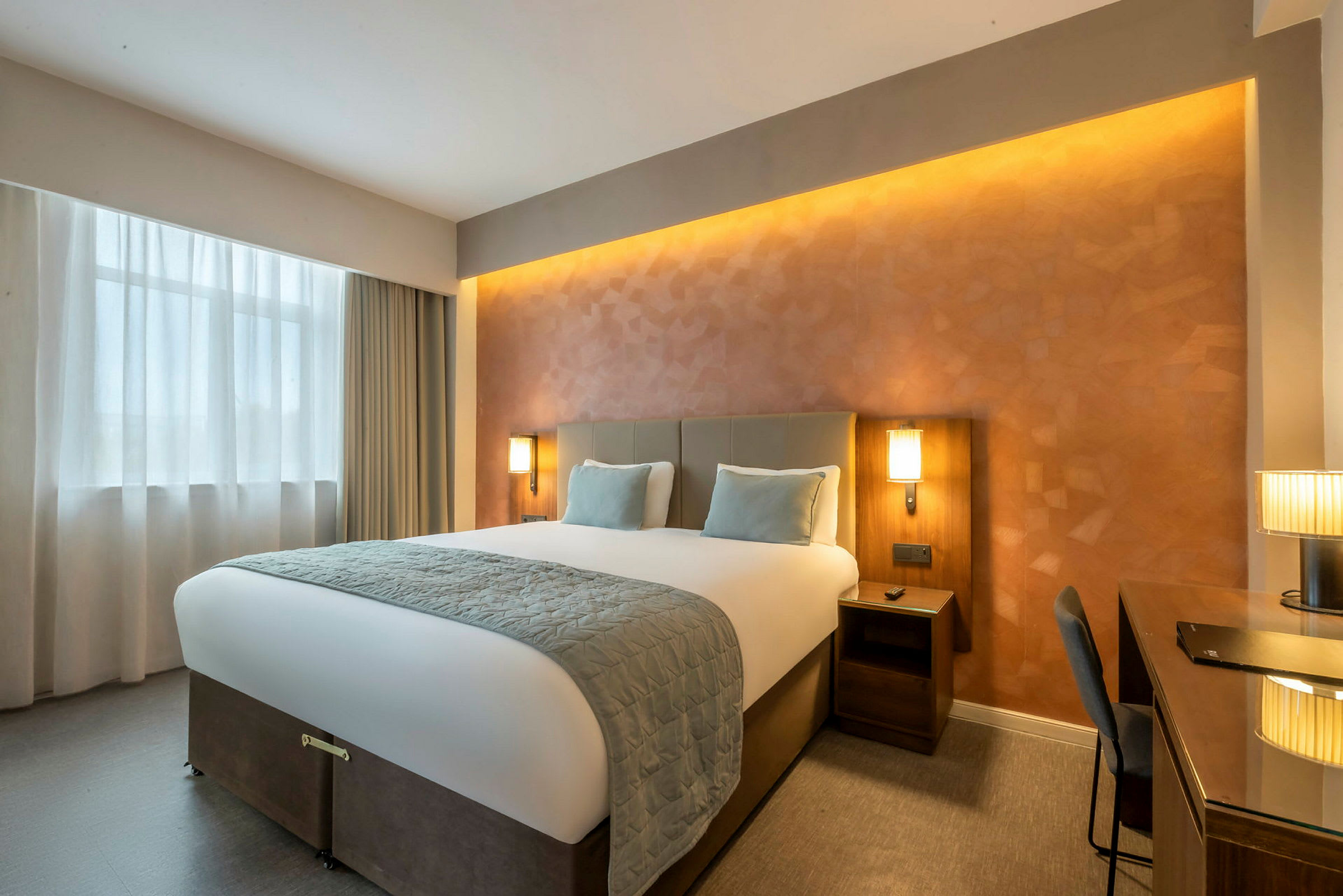 Hotellihuone, jossa on suuri sänky, kaksi yöpöytää ja kirjoituspöytä. (Tekoälyn luoma teksti)