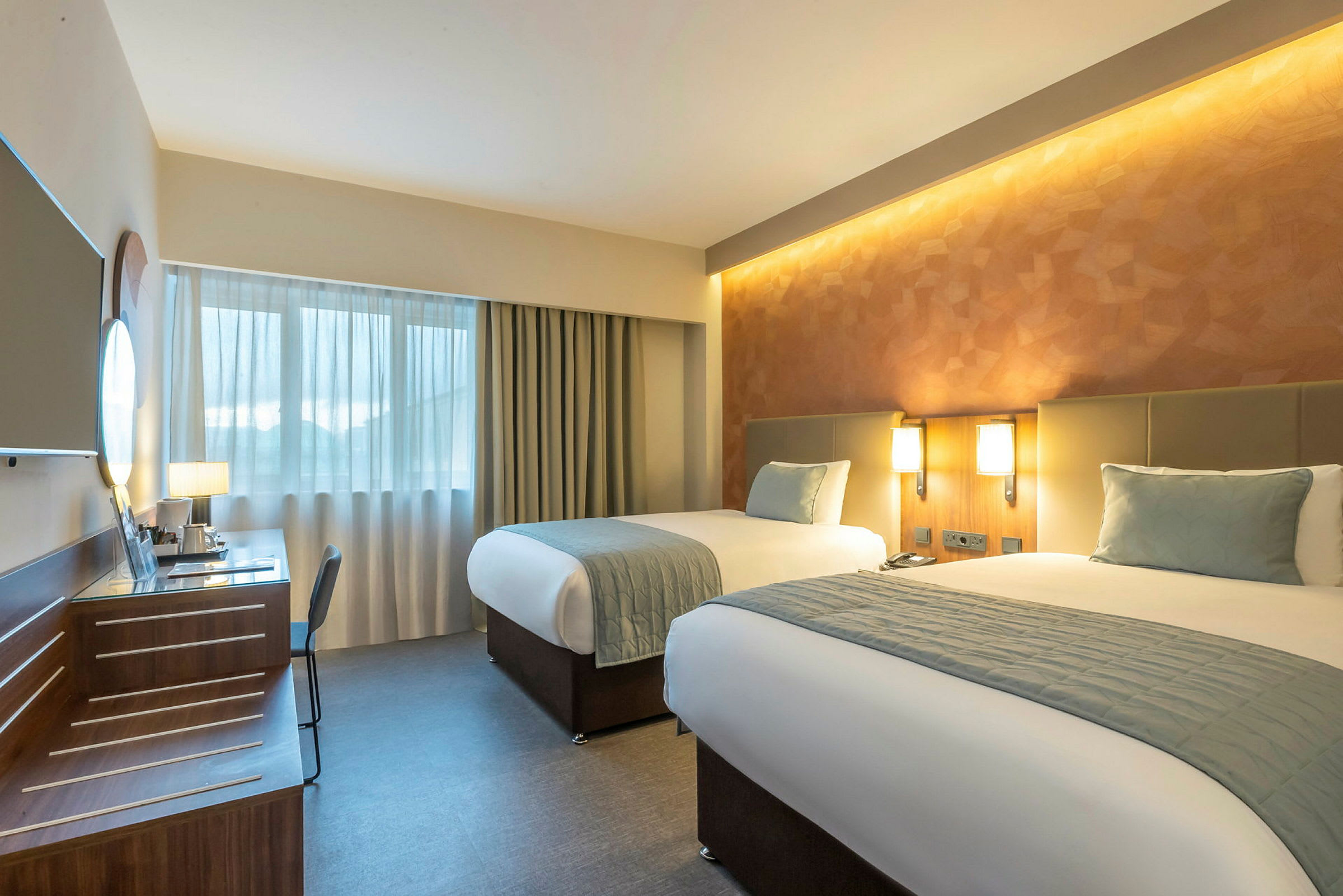 Hotellihuone, jossa on kaksi erillistä sänkyä, kirjoituspöytä ja ikkuna. (Tekoälyn luoma teksti)
